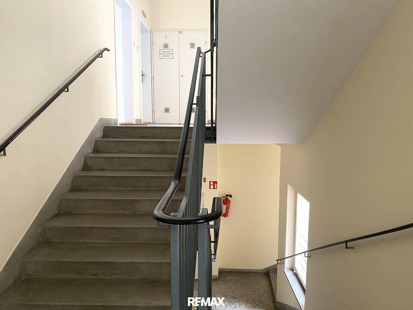 Treppenhaus eines Gebäudes mit Betonstufen und Metallgeländer, gut beleuchtet durch ein Fenster.