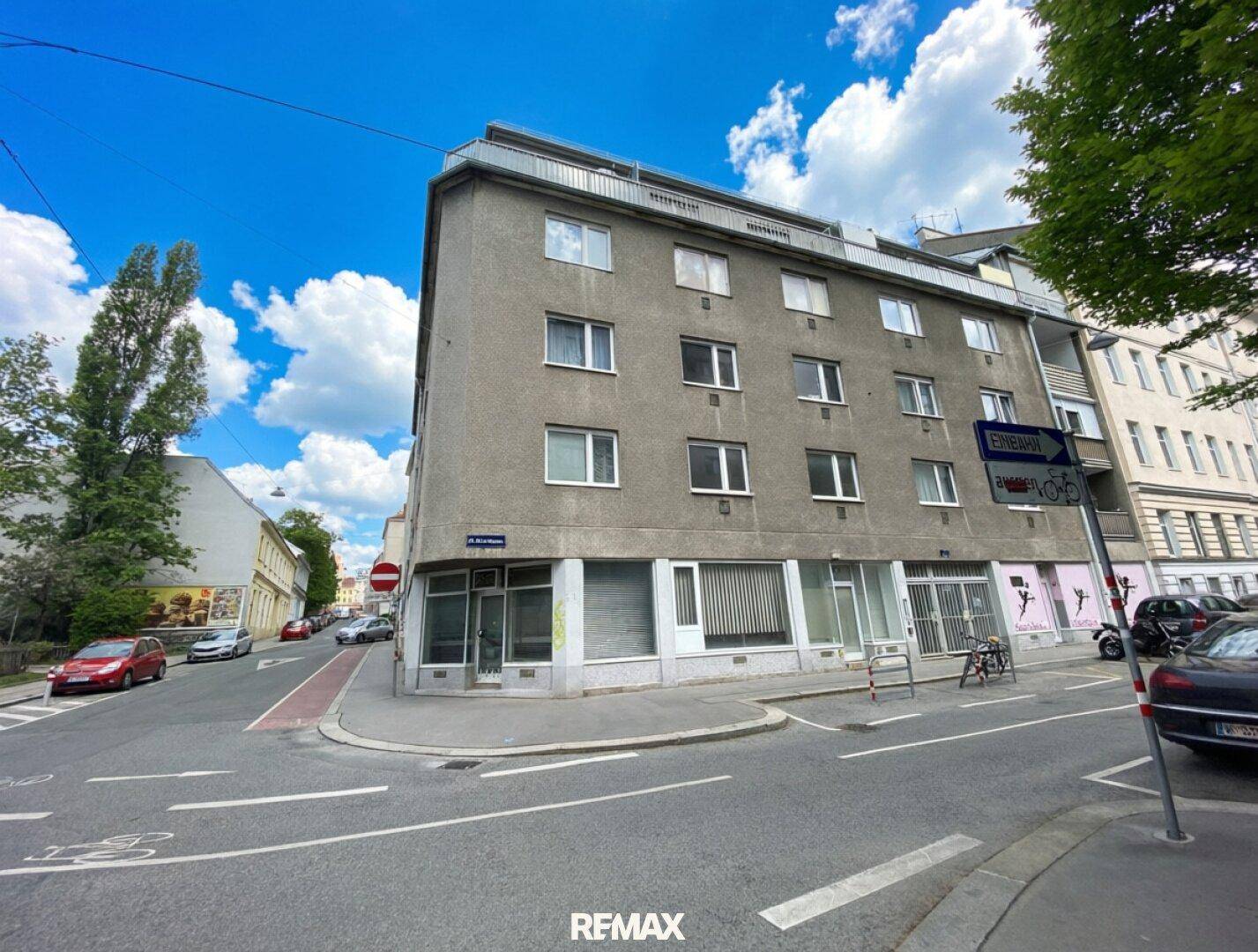 Eckgebäude mit grauer Fassade und mehreren Fenstern an einer städtischen Kreuzung, typische Architektur.