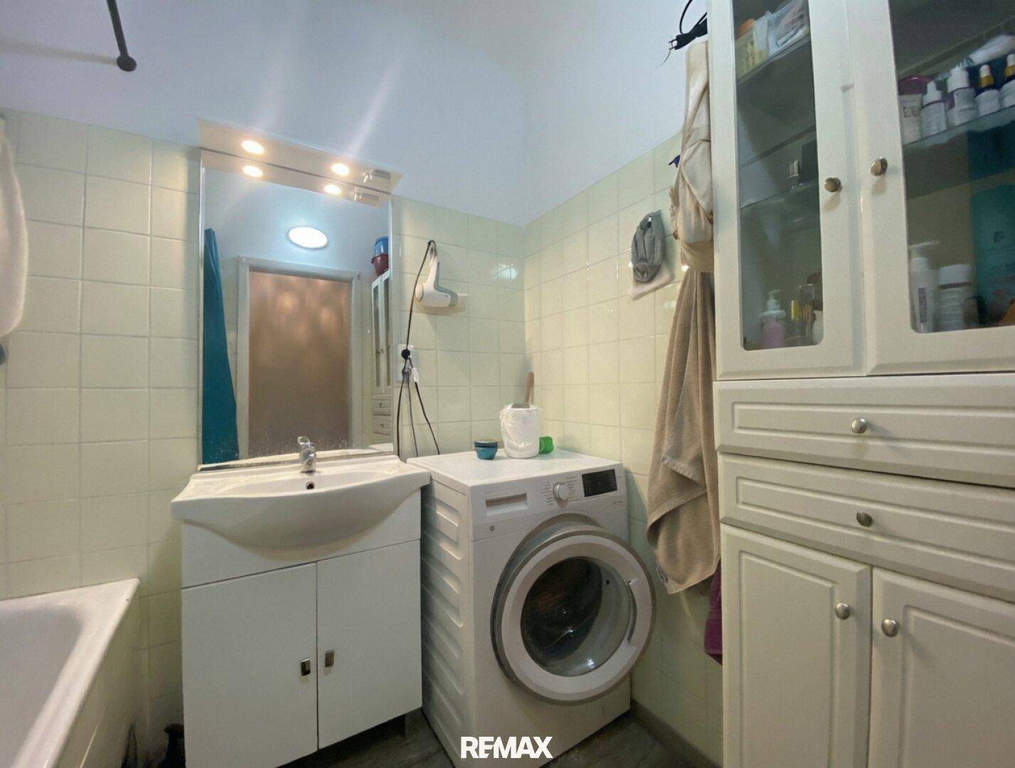 Badezimmer mit Waschbecken, großem Spiegel und praktischer Waschmaschine für den Haushalt.