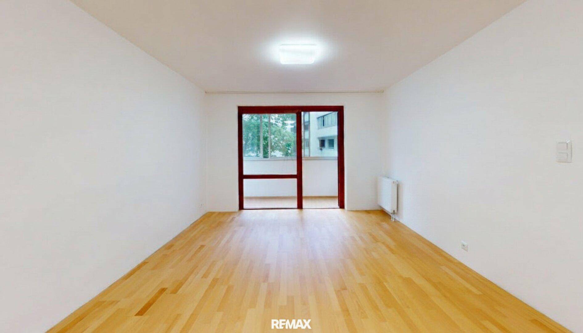 Geräumiges, leeres Zimmer mit hellem Parkettboden und Zugang zu einem Außenbereich.