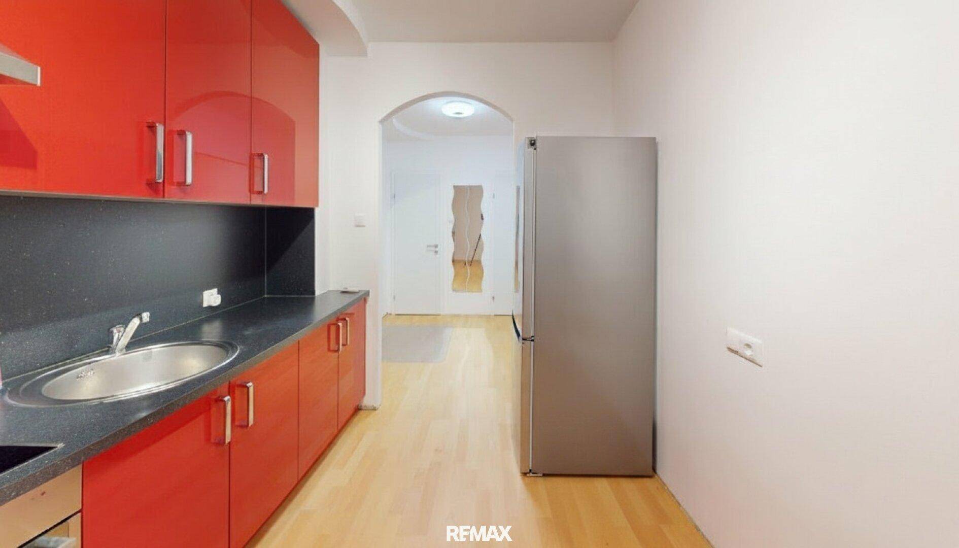 Moderne Küche mit leuchtend roten Schränken, dunkler Arbeitsplatte und Kühlschrank.