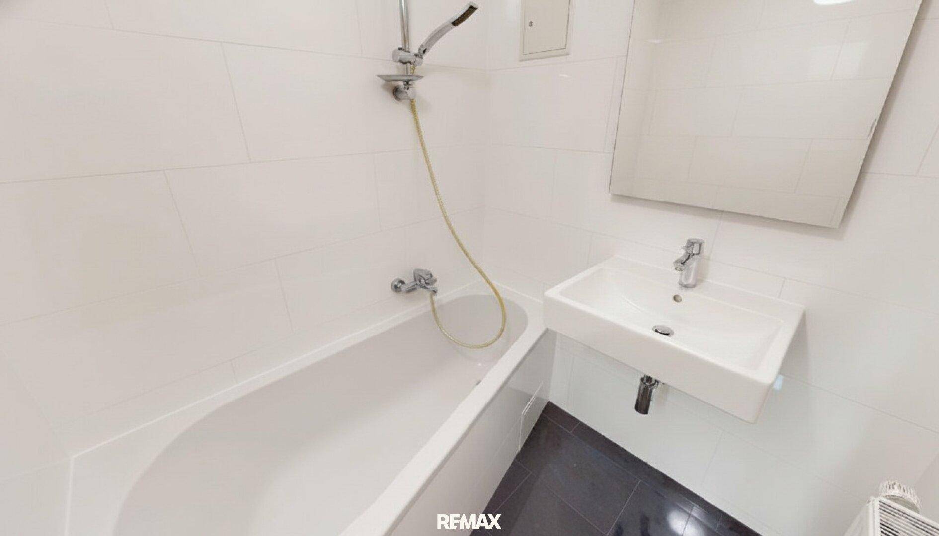 Modernes Badezimmer mit weißen Fliesen, Badewanne mit Duschfunktion und Waschbecken.