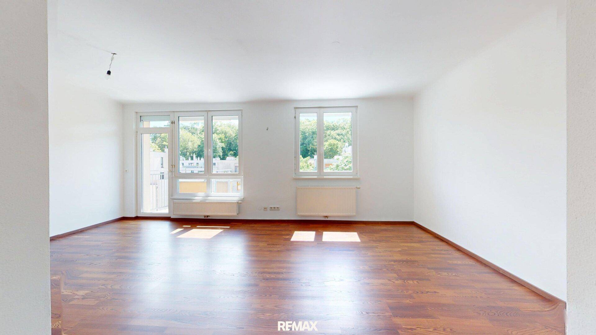Helles Wohnzimmer mit Holzboden und Zugang zu einem Balkon, der viel Tageslicht hereinlässt.