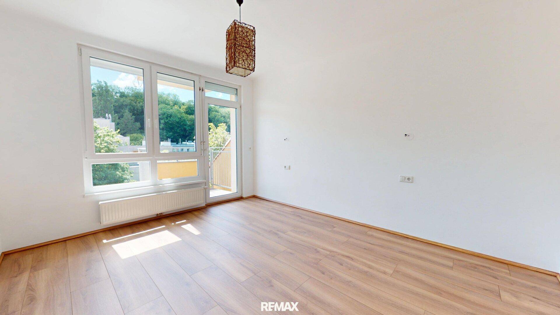 Helles Zimmer mit Holzboden und großem Fenster, das viel Tageslicht hereinlässt.