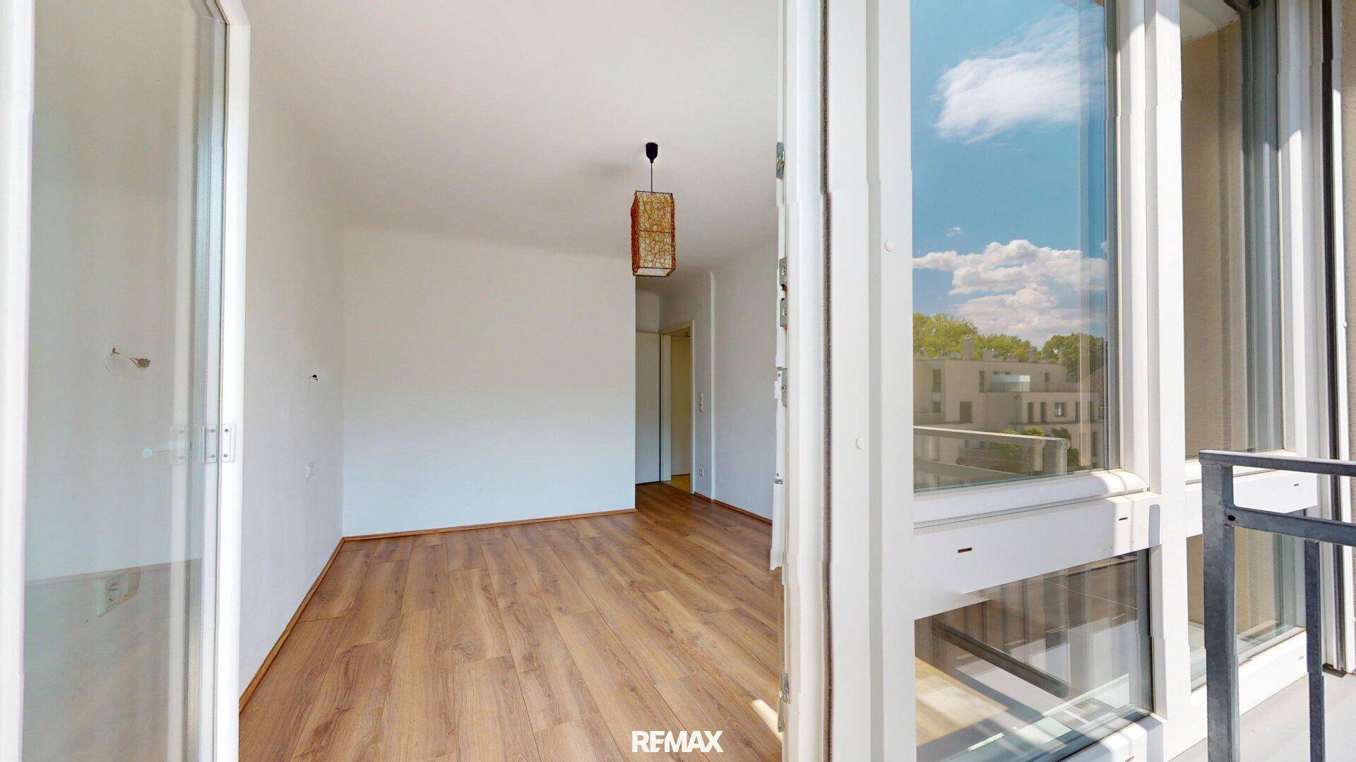 Geräumiges Zimmer mit Zugang zum Balkon, Holzboden und viel natürlichem Licht.