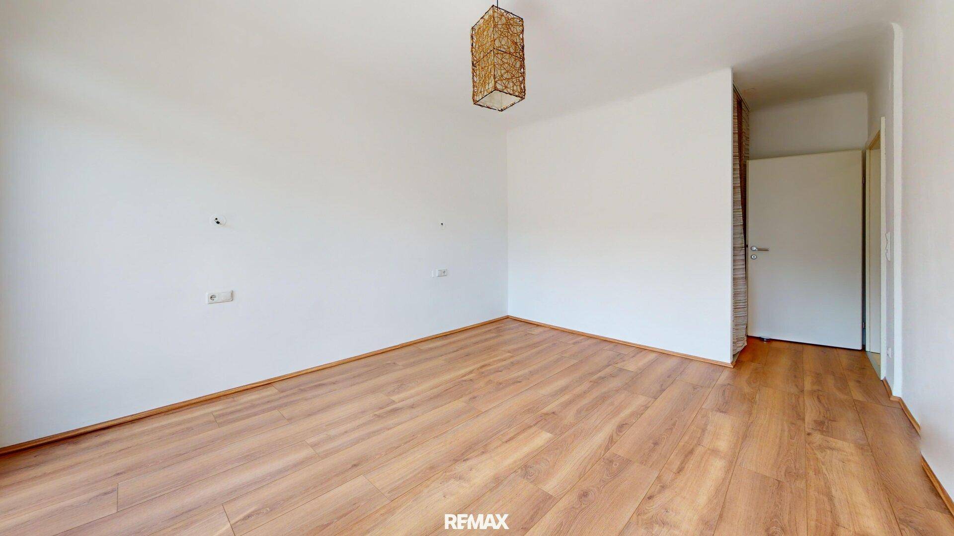 Geräumiges, leeres Zimmer mit Laminatboden und einer modernen Deckenleuchte aus Naturmaterialien.