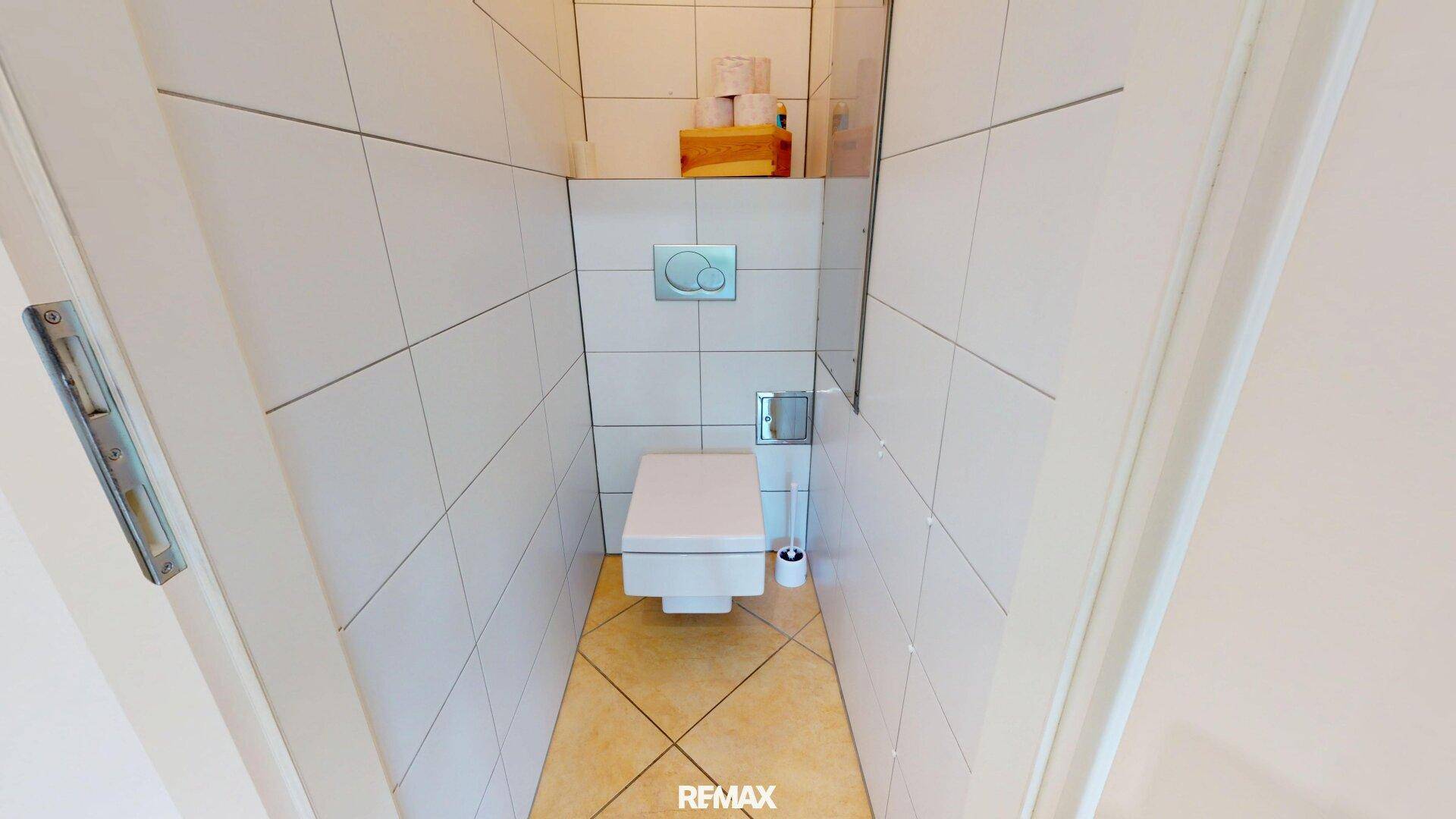 Kleines, hell gefliestes Gäste-WC mit wandhängender Toilette und beigefarbenem Fliesenboden.