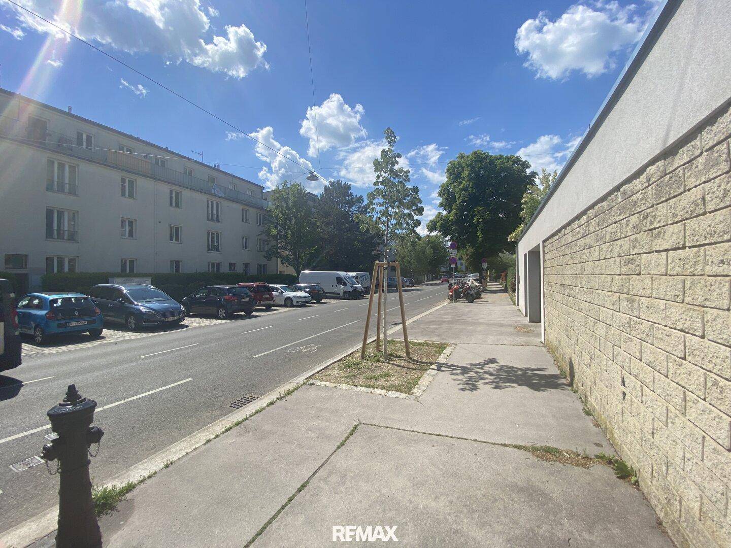 Außenansicht des Gebäudes und der Straße mit parkenden Autos und Bäumen an einem sonnigen Tag.