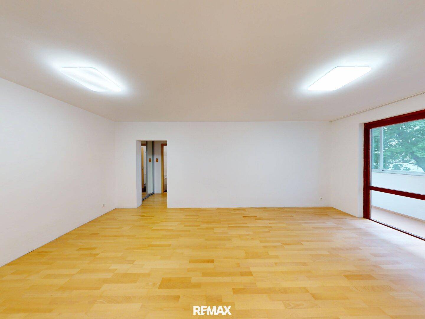 Geräumiger, heller Raum mit Parkettboden und großem Fenster, ideal als Wohnzimmer nutzbar.