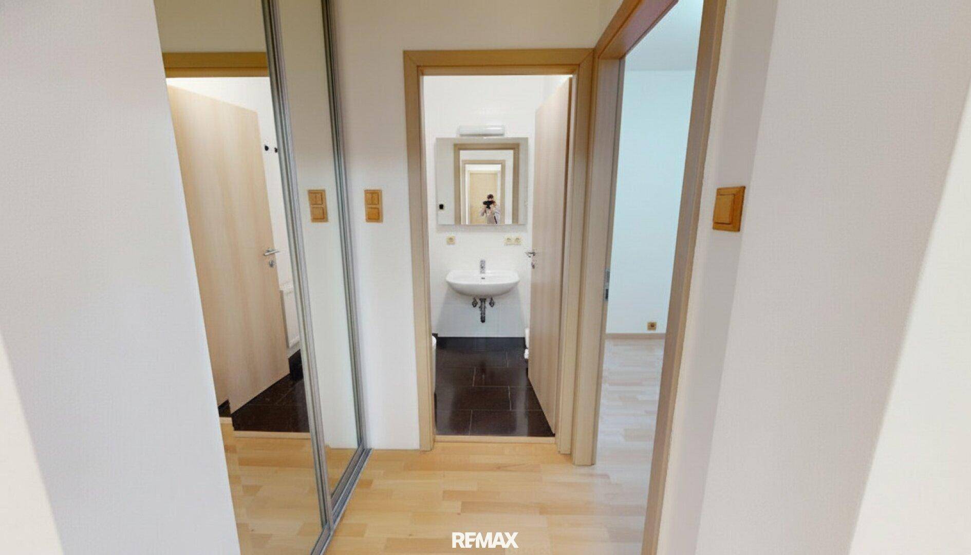 Heller Flur mit Spiegelschränken und Zugang zu einem Badezimmer mit Waschbecken.