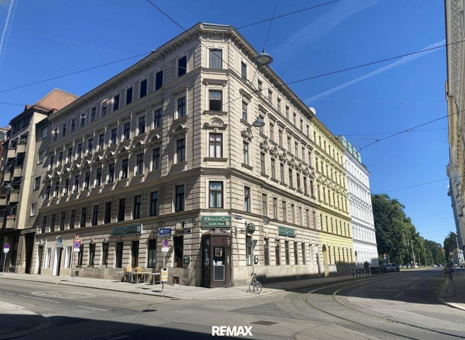 Historisches Eckgebäude in der Stadt mit klassischer Architektur und Geschäften im Erdgeschoss unter blauem Himmel.