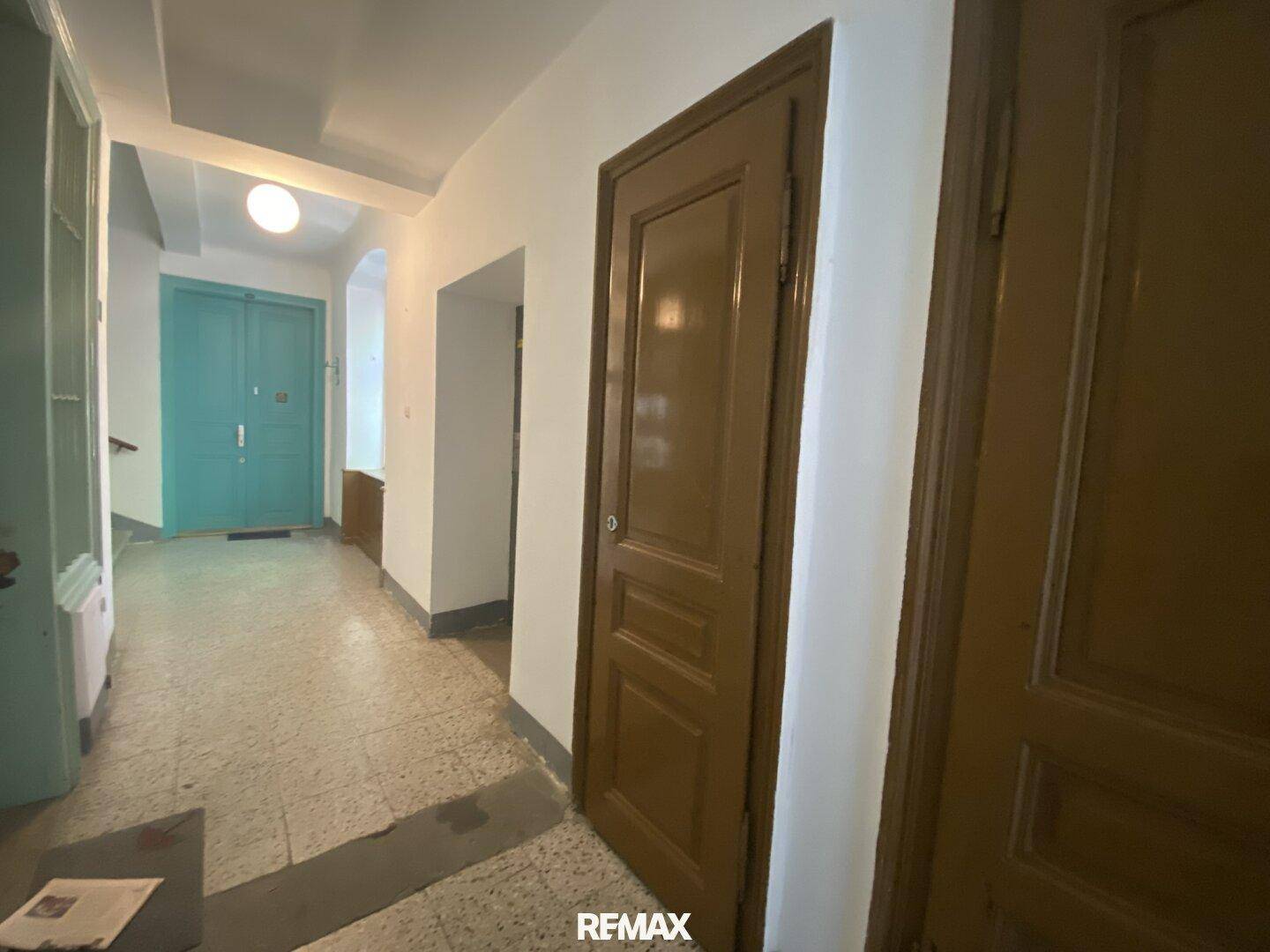 Gemeinschaftlicher Flur in einem Altbau mit Terrazzoboden und mehreren Holztüren, die zu den Wohnungen führen.