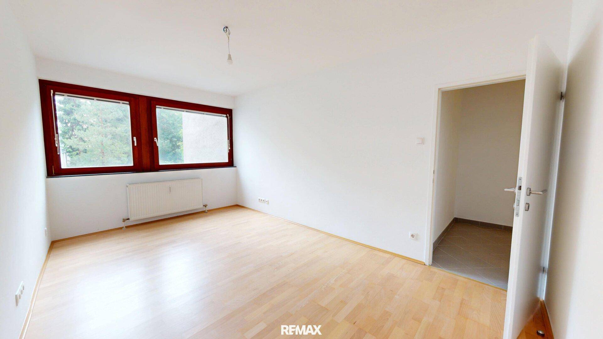 Leeres Zimmer mit Holzboden und großen Fenstern, ideal als Schlafzimmer nutzbar.