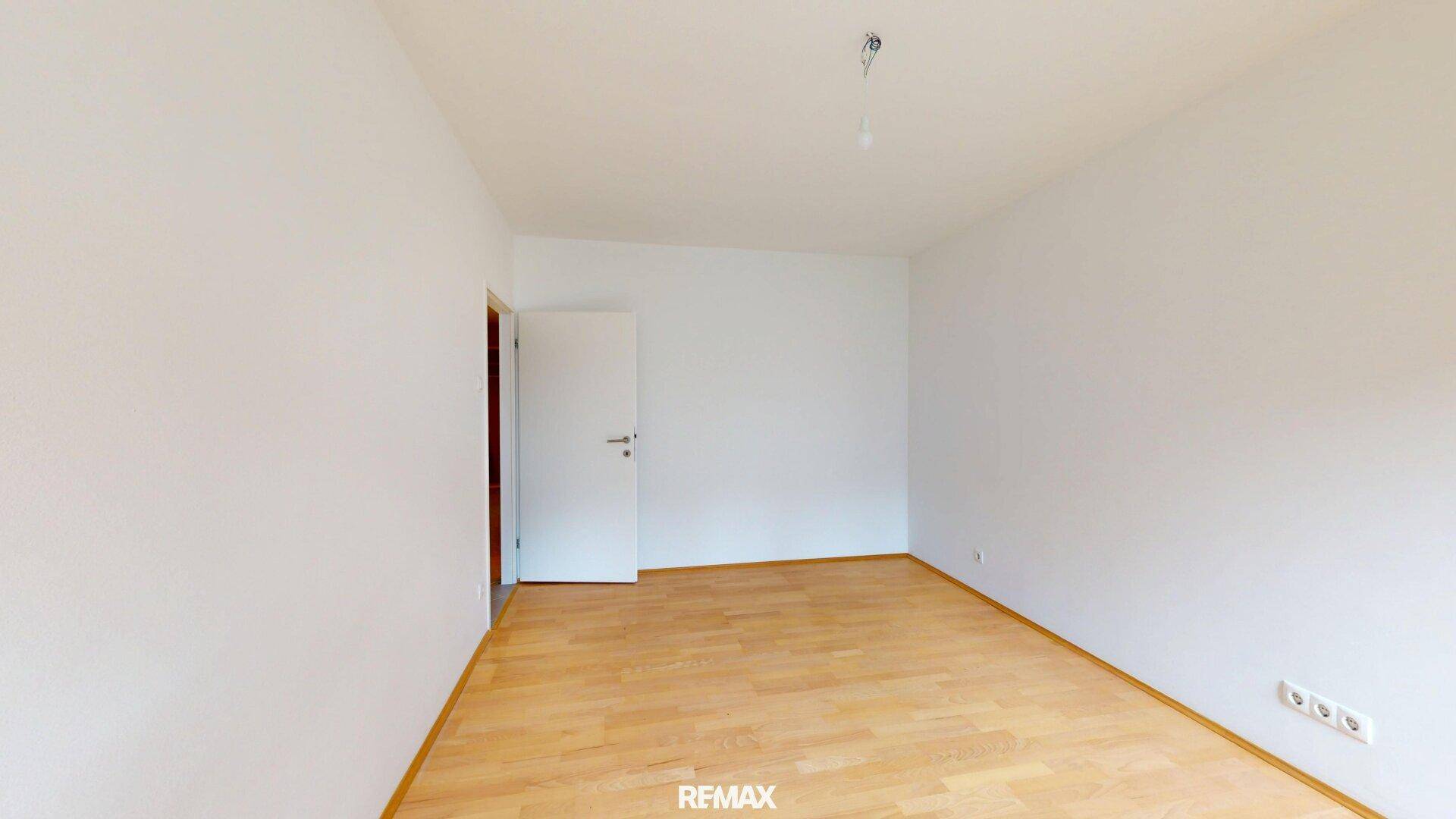 Schlichter Raum mit Parkettboden und einer weißen Tür, ideal als Schlaf- oder Arbeitszimmer nutzbar.