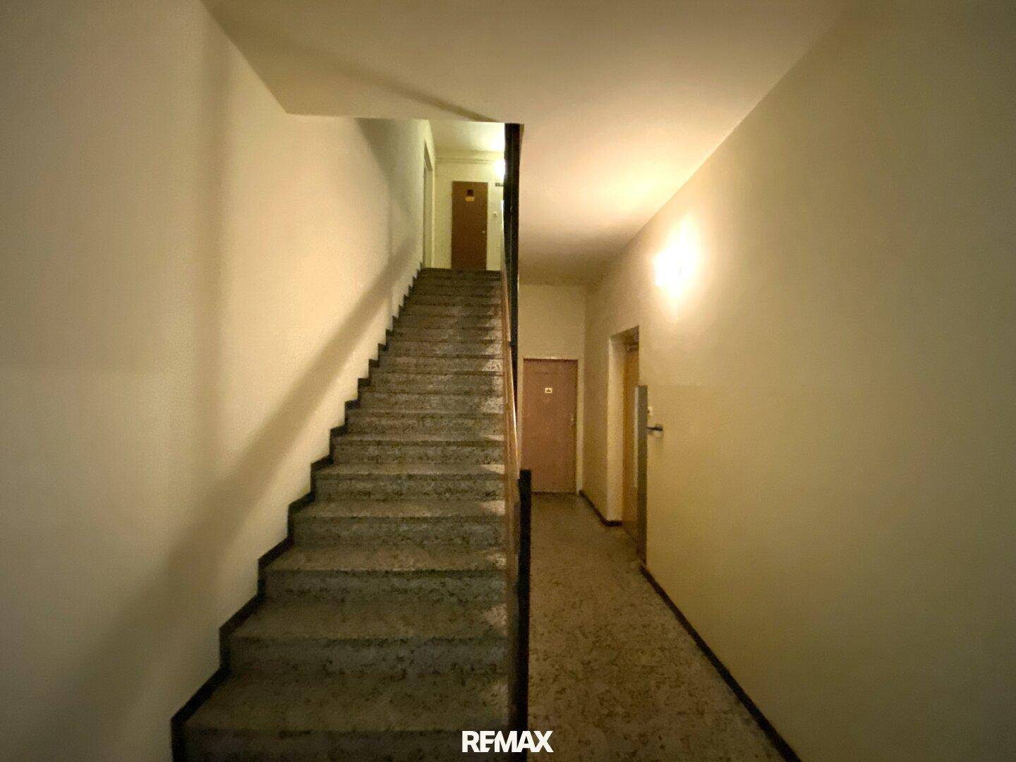 Treppenhaus mit Steinstufen und einem langen Flur in einem Mehrfamilienhaus.