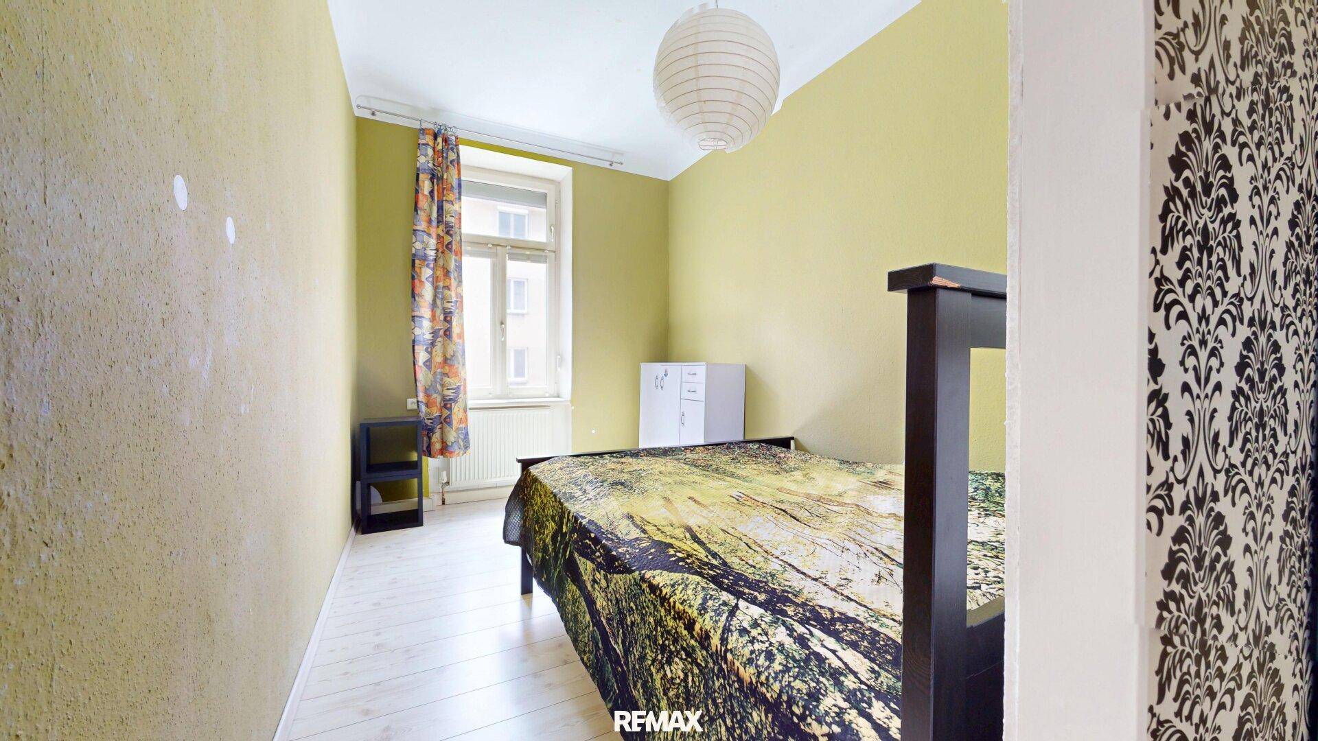 Schlafzimmer mit hellgrünen Wänden, Einzelbett und Fenster, das viel Tageslicht hereinlässt.