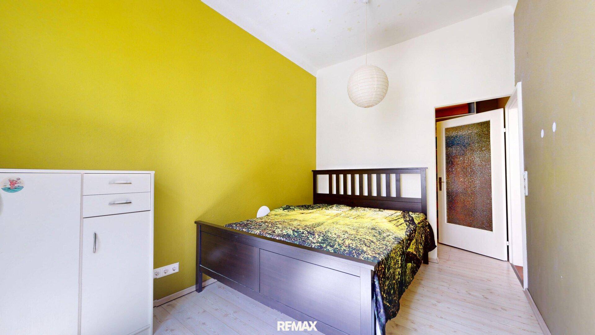 Helles Schlafzimmer mit gelber Akzentwand, Holzbett und praktischem Kleiderschrank.