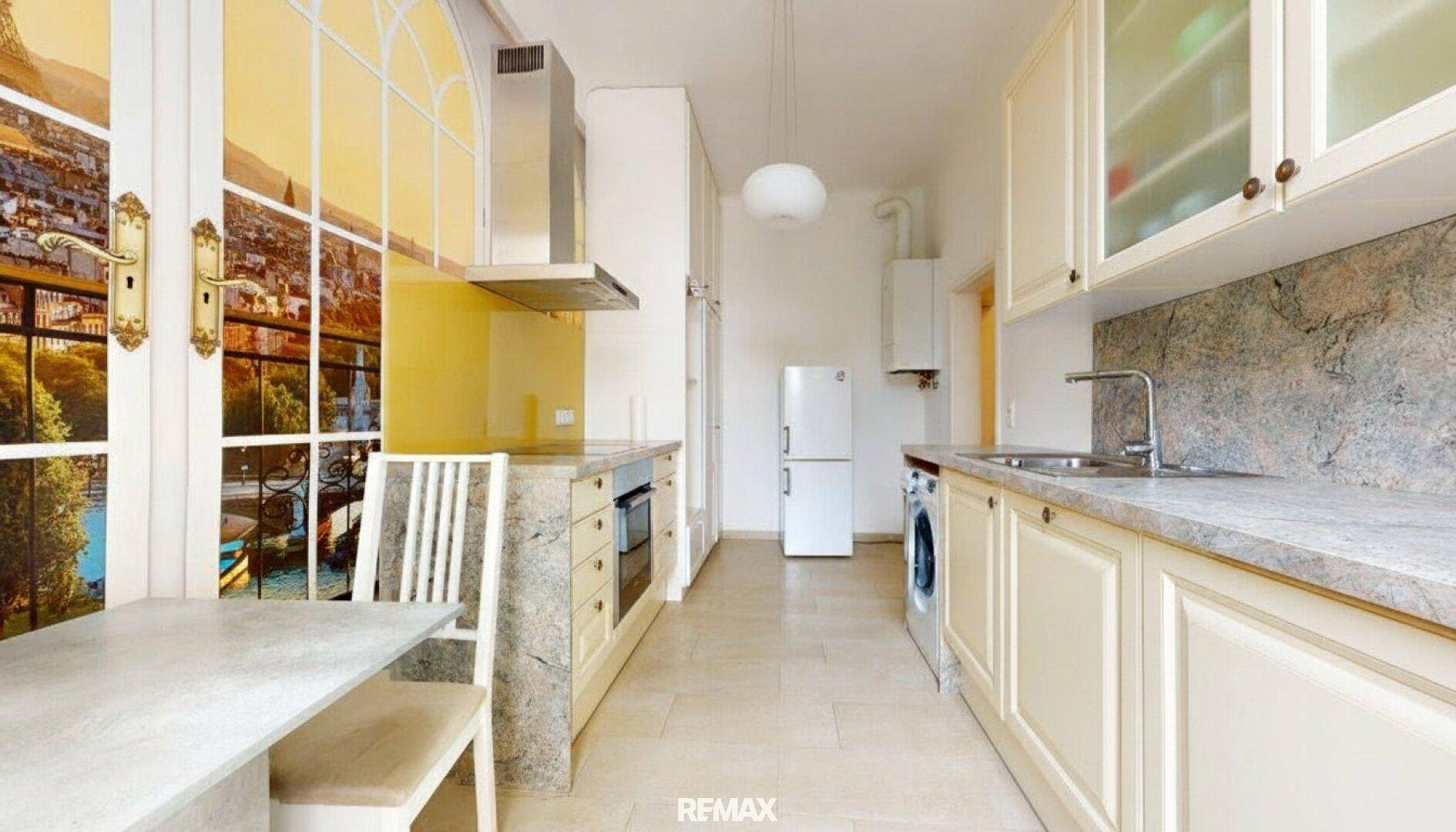 Lange Küche mit Einbauküche, Kühlschrank, Waschmaschine und großem Fenster mit Stadtansicht.