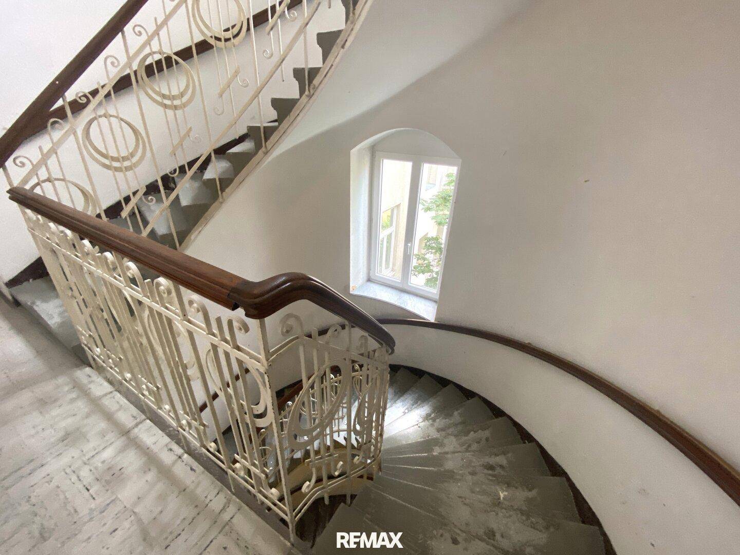 Elegantes Treppenhaus mit geschwungener Treppe, kunstvollem Geländer und Fenster.