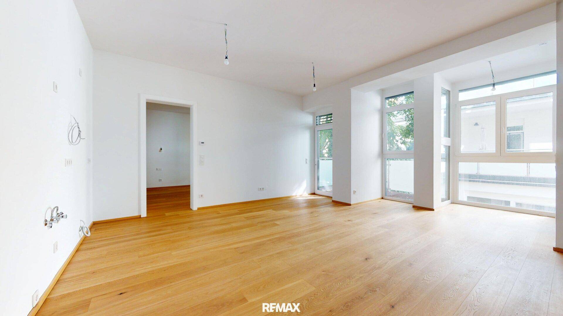 Geräumiger, heller Wohnbereich mit Eichenparkett und Zugang zu einem Balkon.
