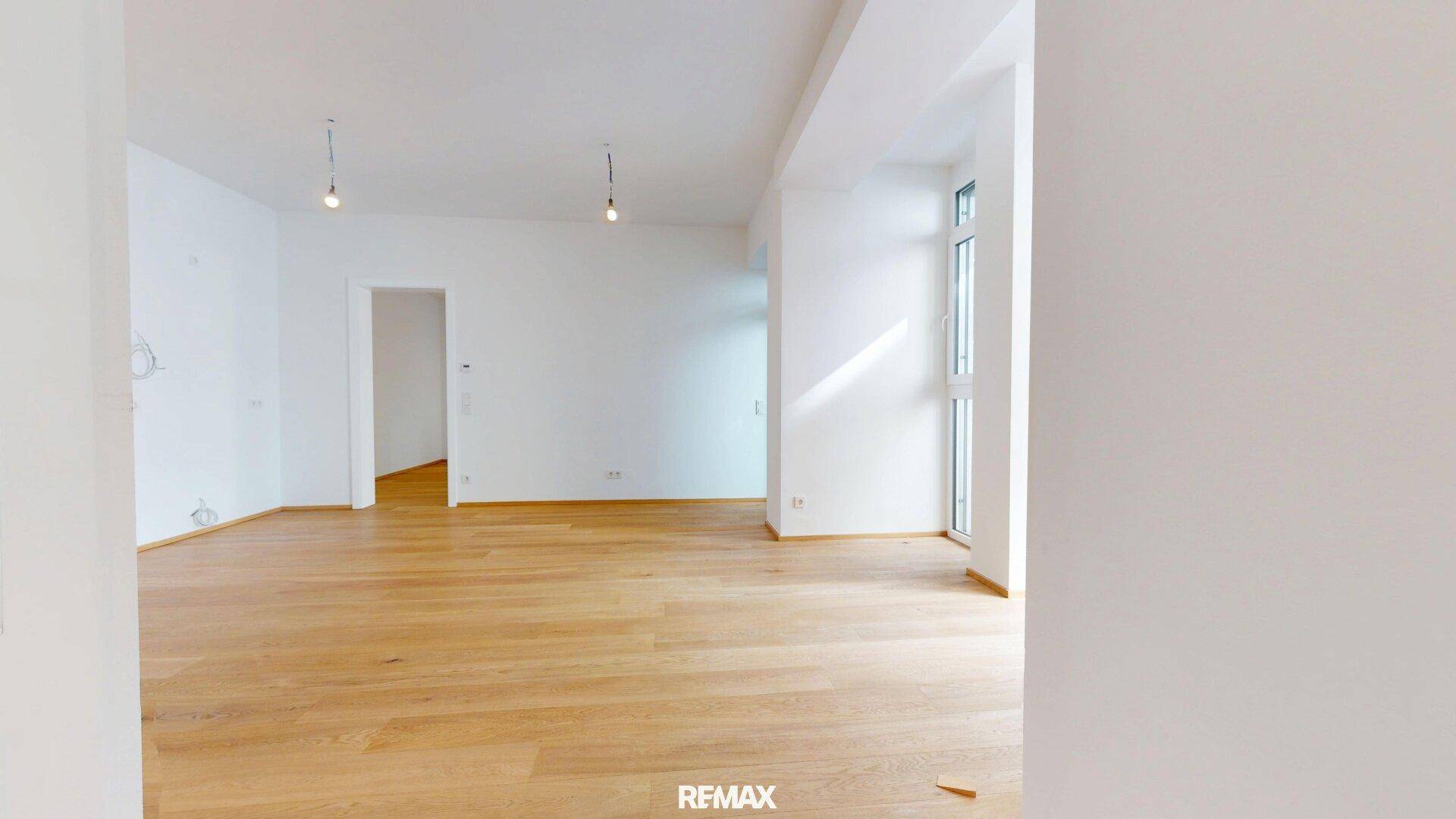 Heller, leerer Raum mit Holzboden und hohen Fenstern, die eine angenehme Atmosphäre schaffen.