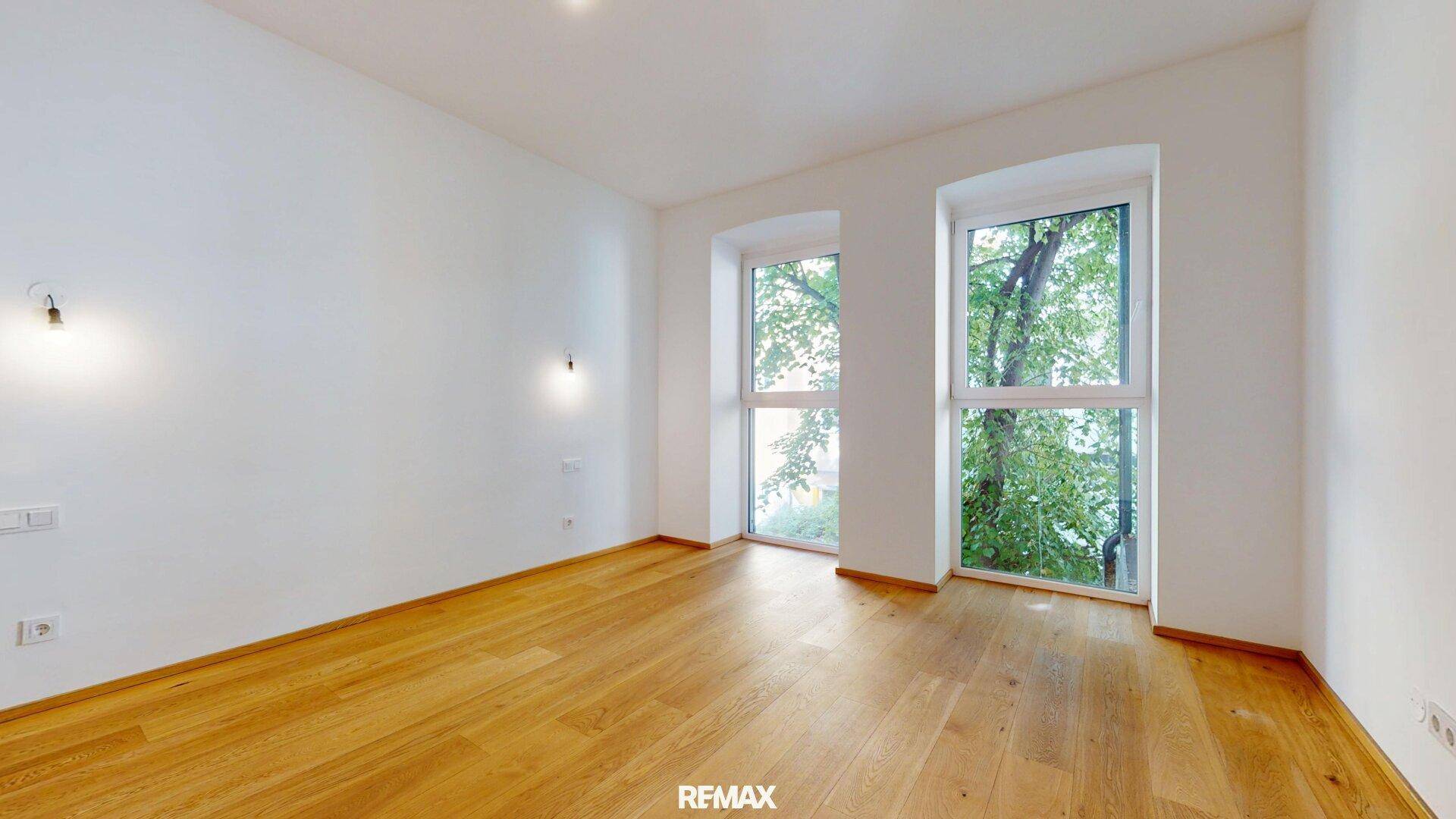 Ruhiges Schlafzimmer mit Holzboden und zwei Fenstern, die einen Blick ins Grüne bieten.