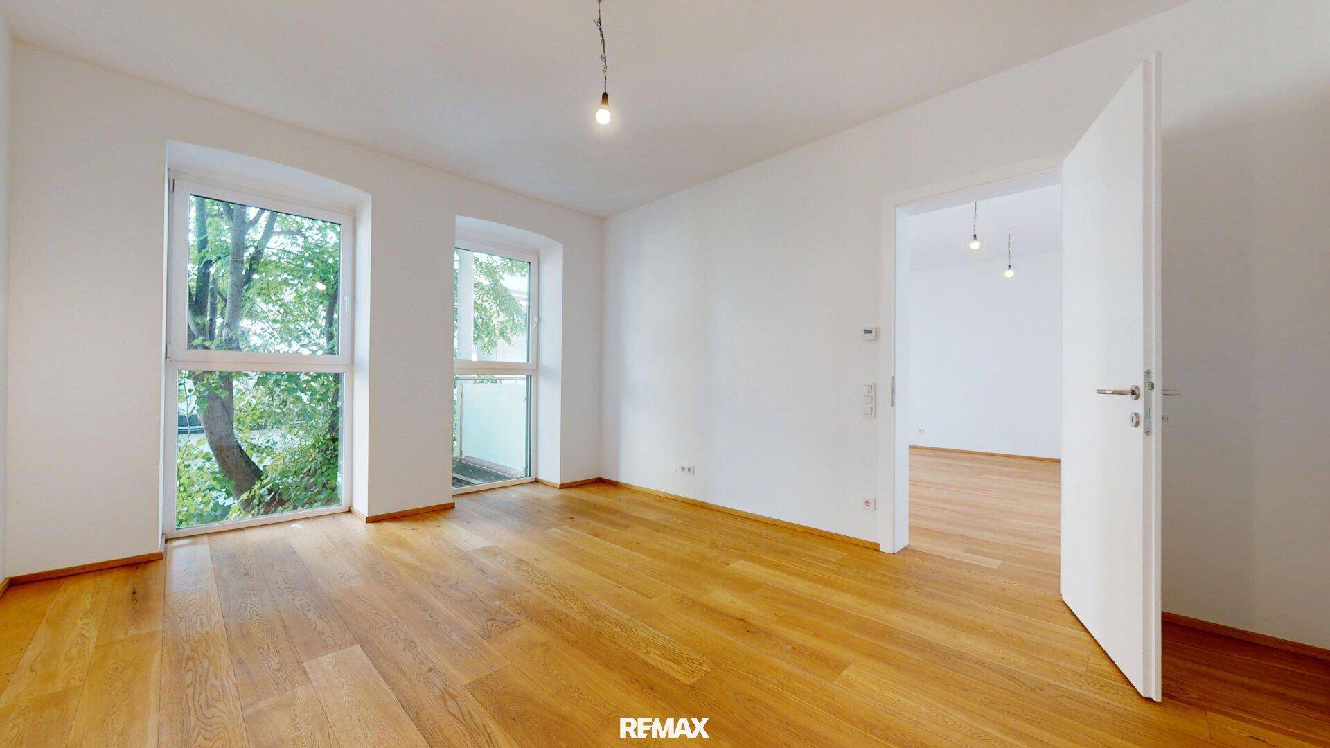 Helles Schlafzimmer mit Holzboden, großen Fenstern und direktem Zugang zum Balkon.