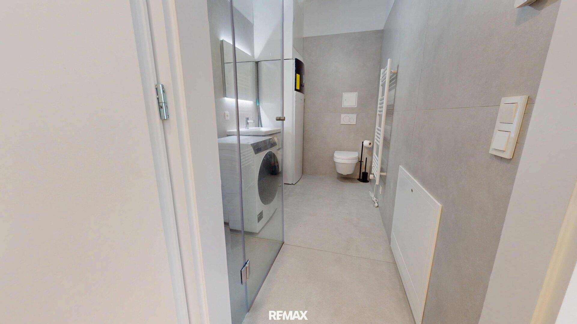 Eingangsbereich zum modernen Badezimmer mit grauen Fliesen und zeitgemäßer Ausstattung.