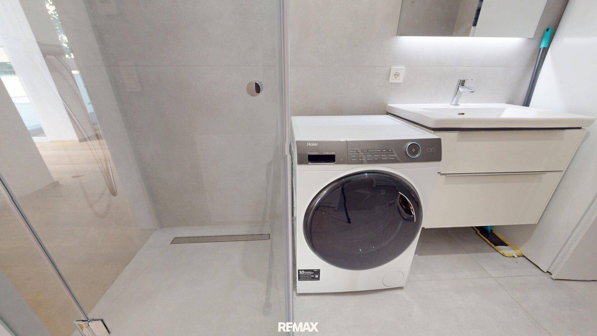 Detaillierte Ansicht des modernen Badezimmers mit begehbarer Dusche, Waschbecken und Waschmaschine.