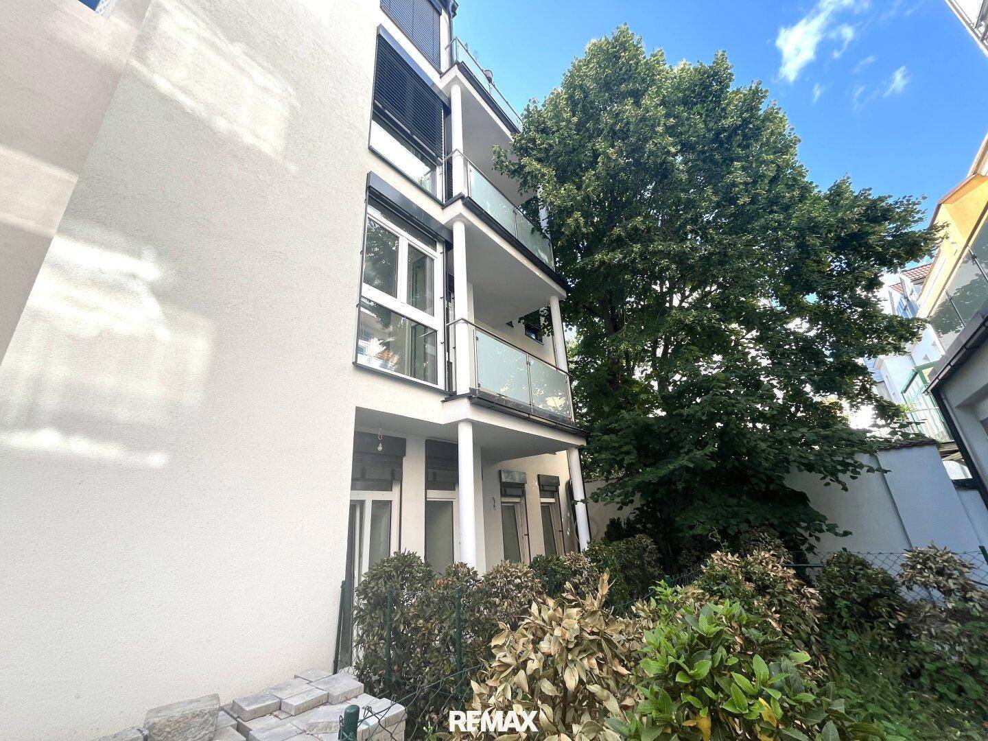 Moderne Gebäudefassade mit mehreren Balkonen und umgebenden Bäumen.