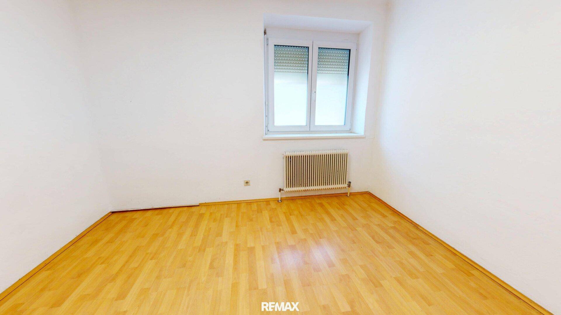 Schlichter Raum mit Holzfußboden und einem Fenster, bereit zur individuellen Gestaltung.