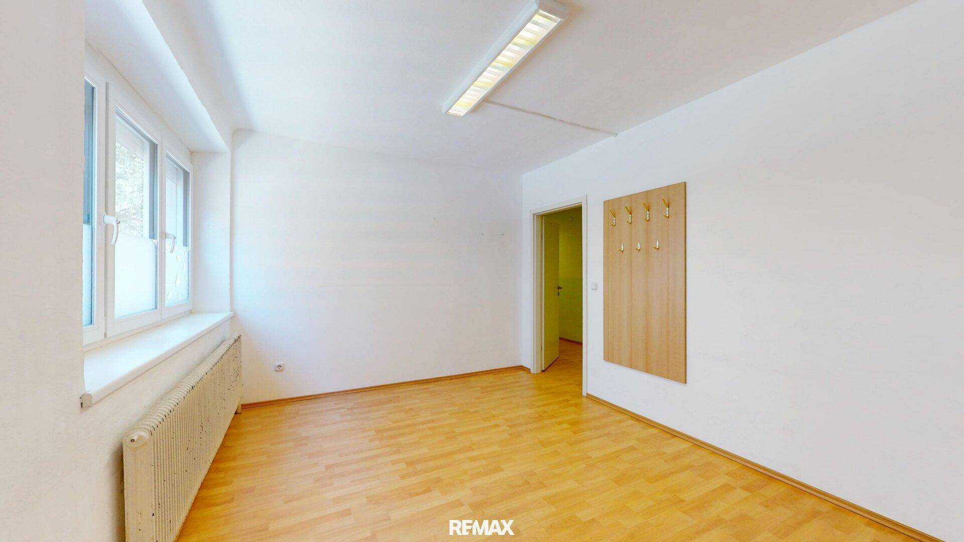 Heller Raum mit Holzfußboden, großem Fenster und Garderobe, vielseitig nutzbar.