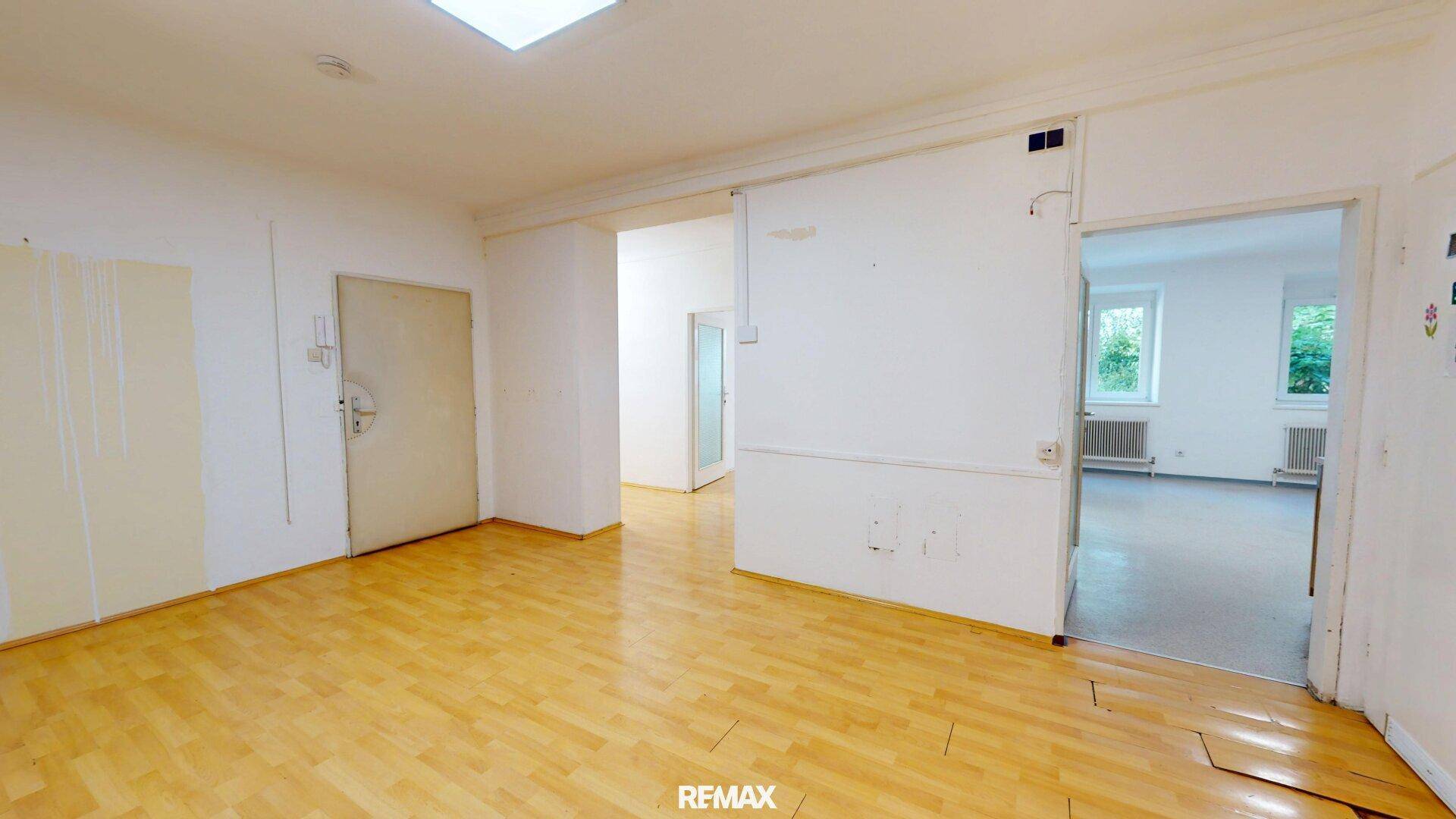 Großer, offener Raum mit Holzfußboden und Blick in angrenzende Zimmer.
