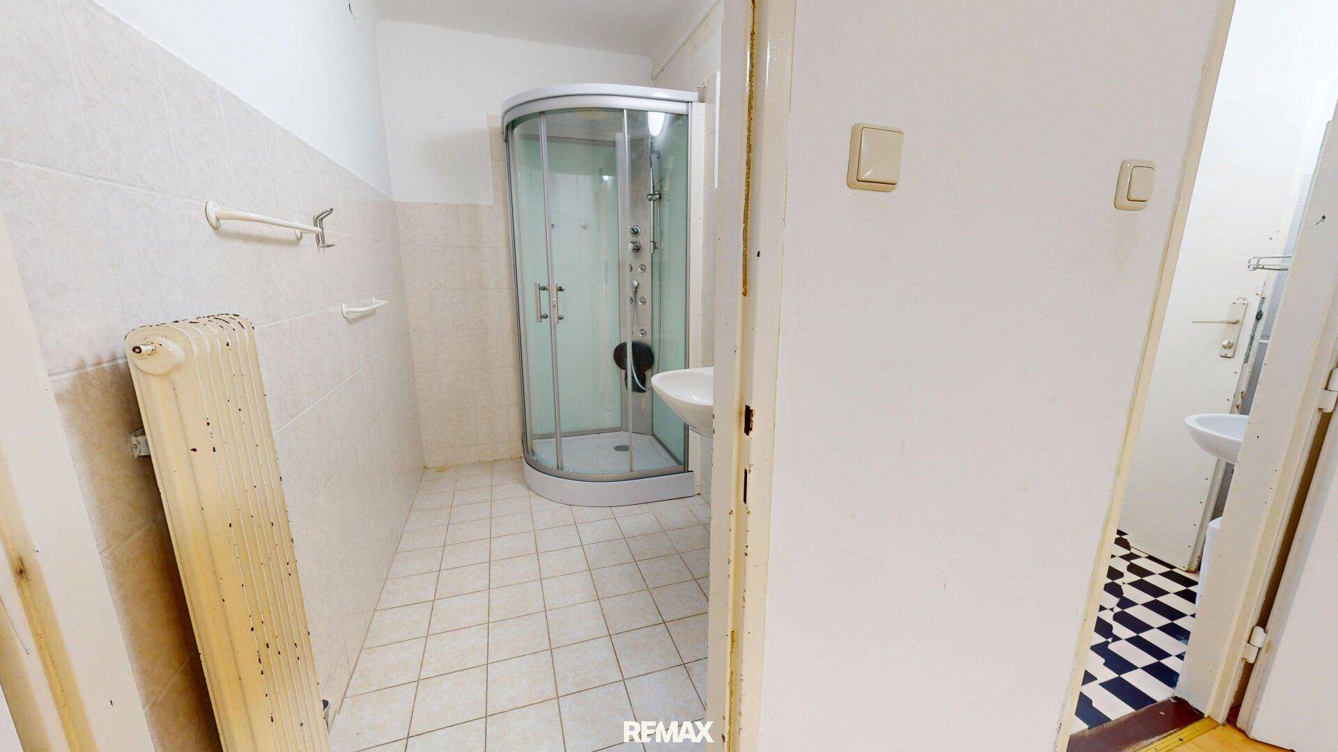 Badezimmer mit Duschkabine, Waschbecken und Fliesenboden, funktional eingerichtet.