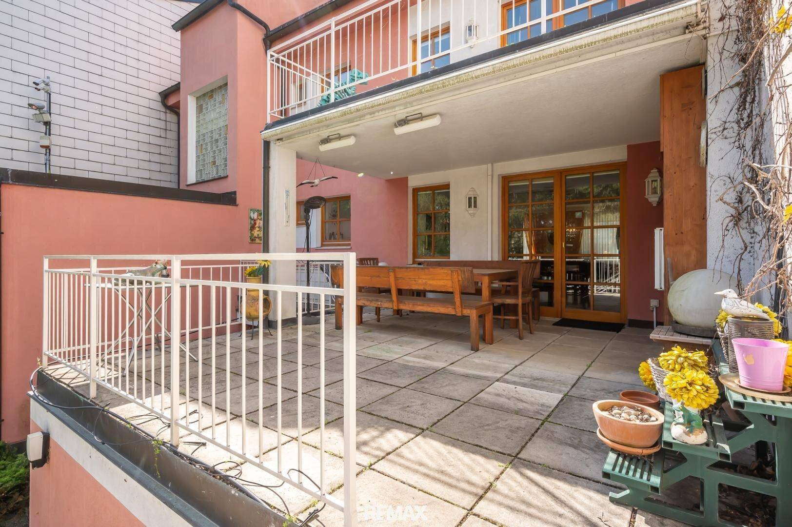 Große geflieste Terrasse mit Holzbänken und Zugang zum Gartenbereich des Hauses.