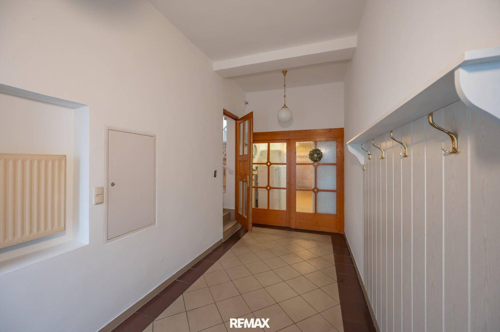 Geräumiger Flur mit Fliesenboden, Holzinnentüren und praktischer Wandgarderobe.