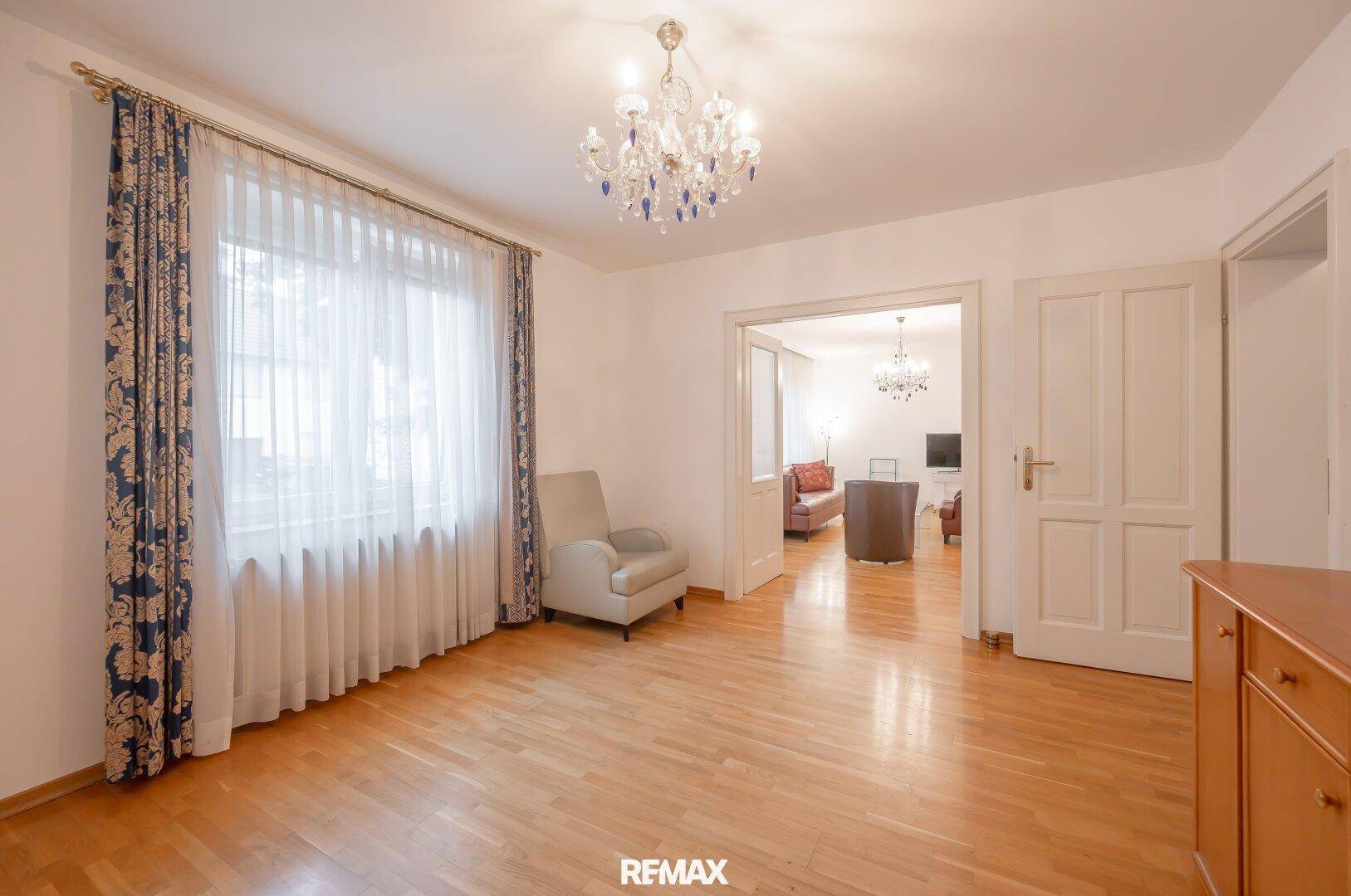 Helles Zimmer mit Parkettboden, großem Fenster und klassischem Kronleuchter.
