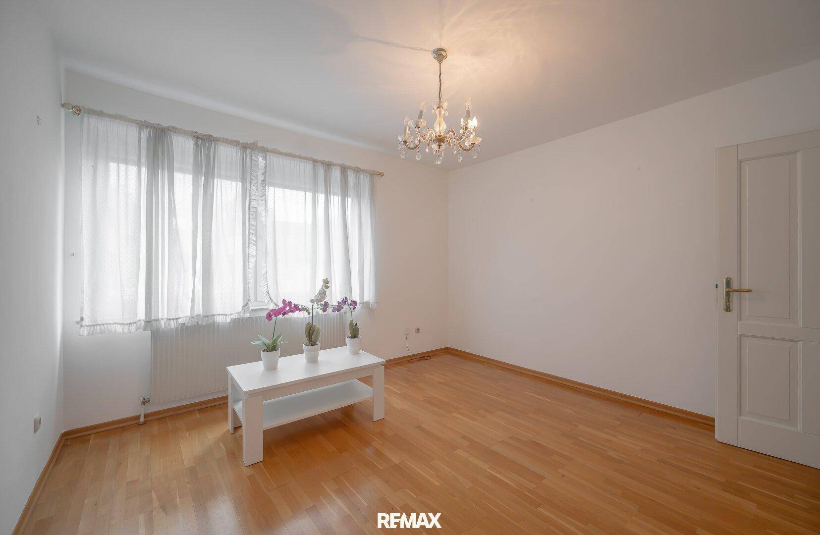 Helles Zimmer mit Parkettboden, großem Fenster und schlichtem Couchtisch.