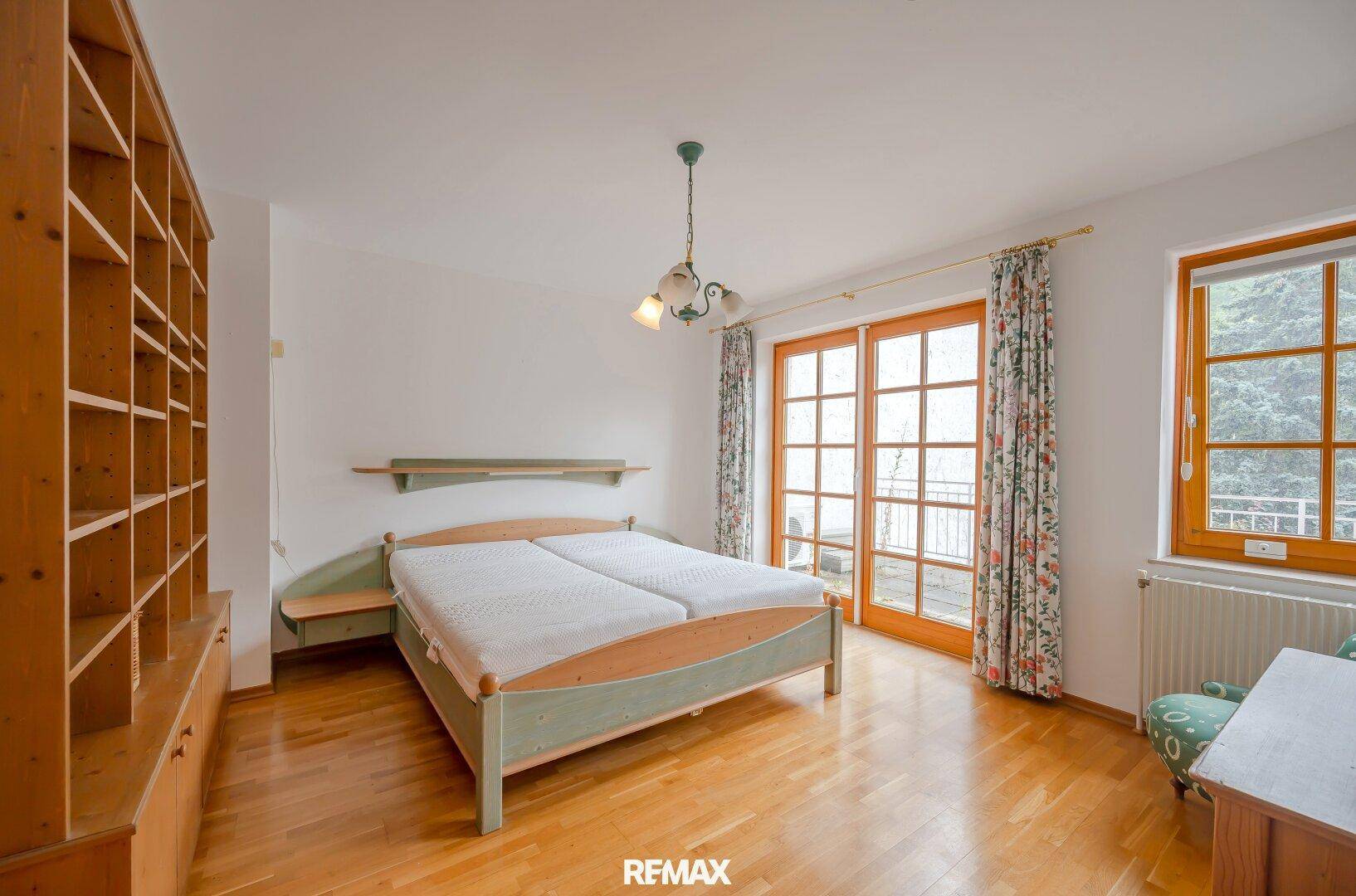 Schlafzimmer mit Holzboden, Doppelbett, Einbauregal und Balkonzugang.