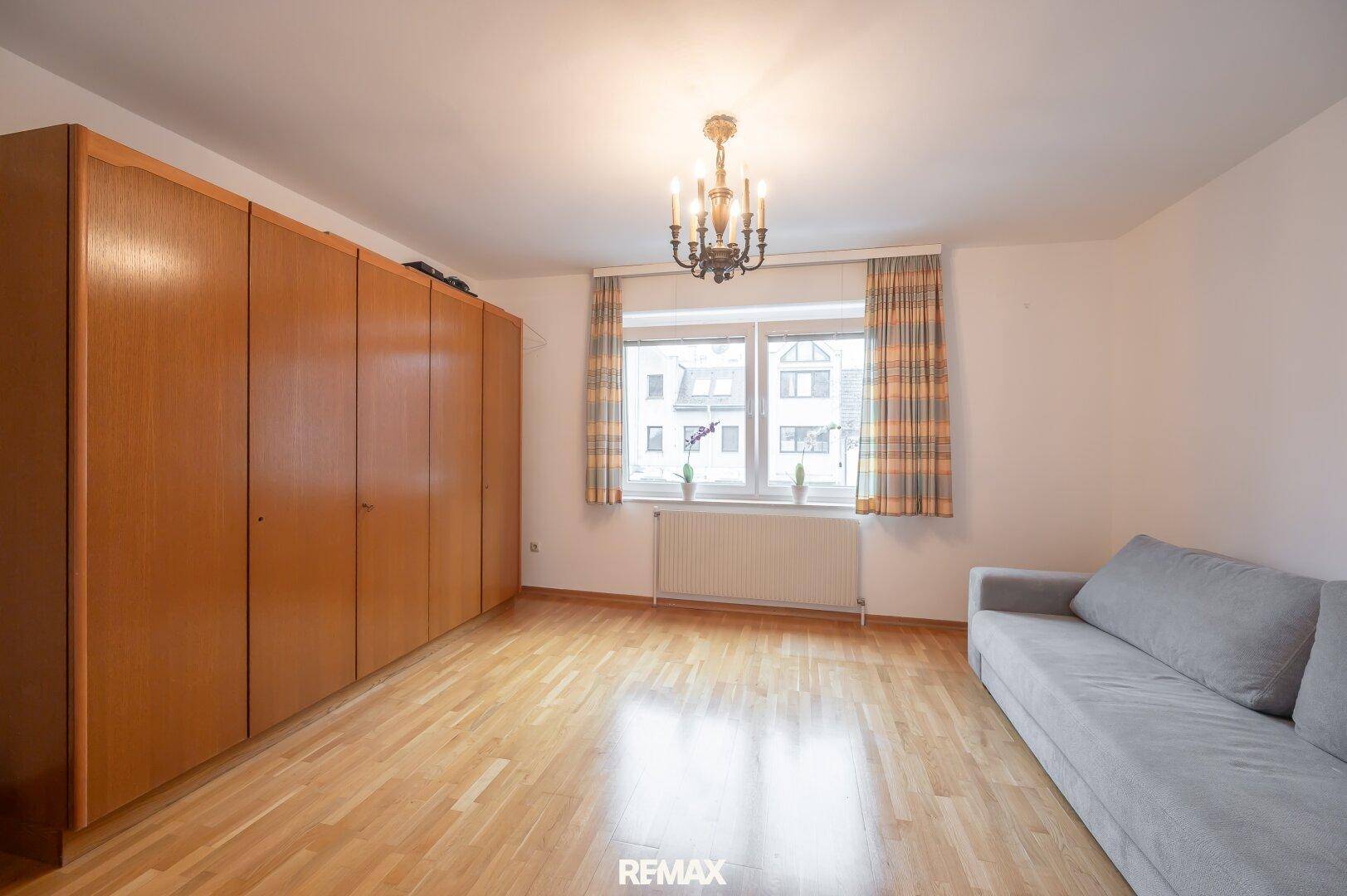 Schlafzimmer mit Parkettboden, großem Kleiderschrank und Fenster mit Blick nach draußen.