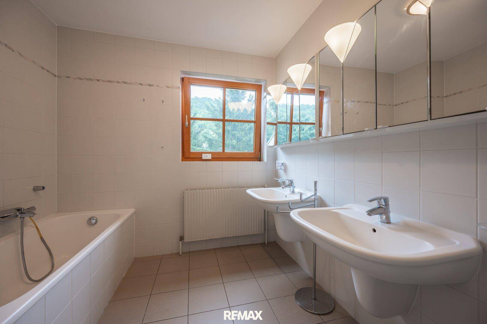 Badezimmer mit zwei Waschbecken, Badewanne, Fliesen und Fenster.