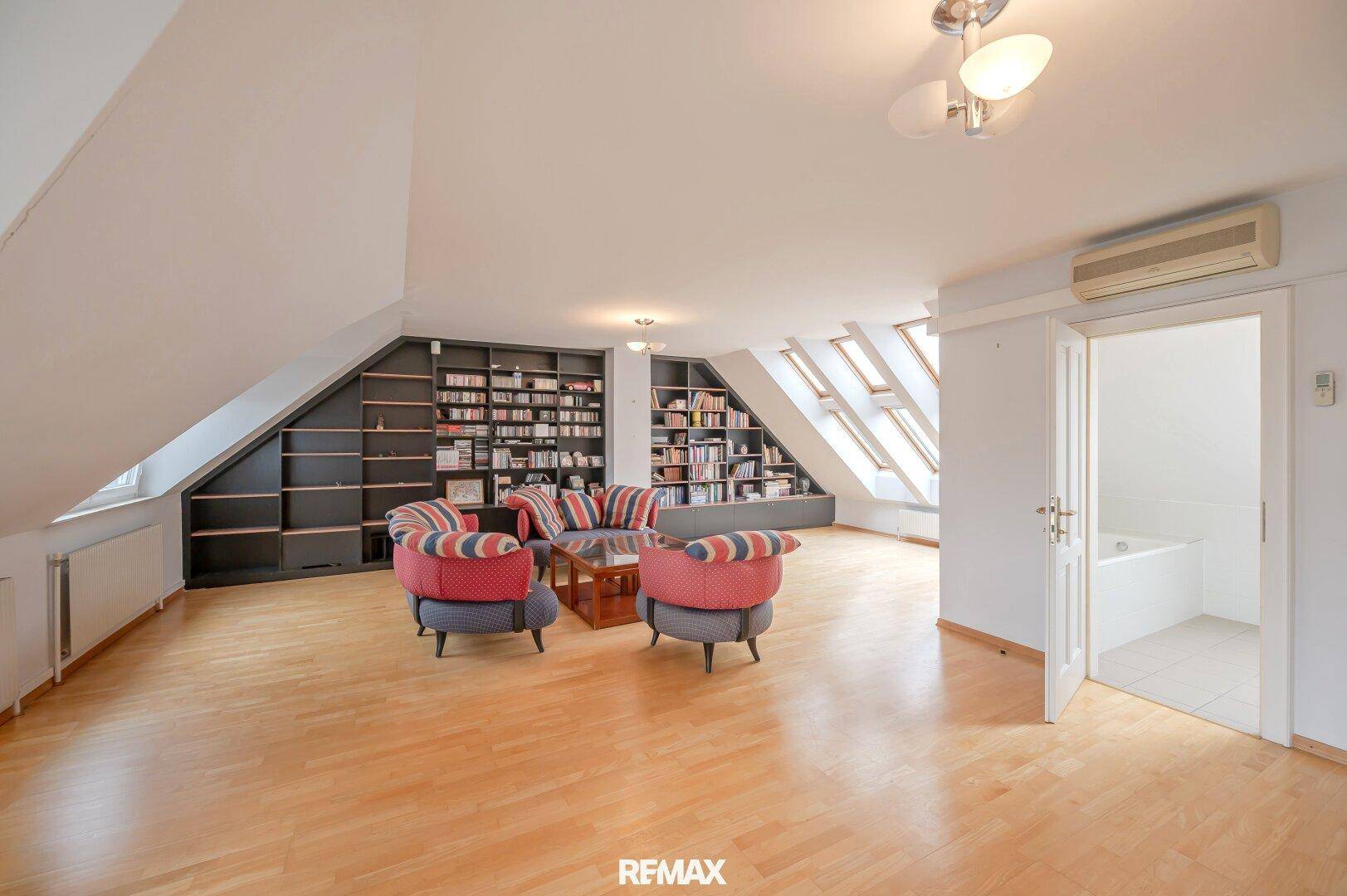 Großes Dachgeschoss-Wohnzimmer mit Holzboden, Einbauregalen und Dachfenstern.