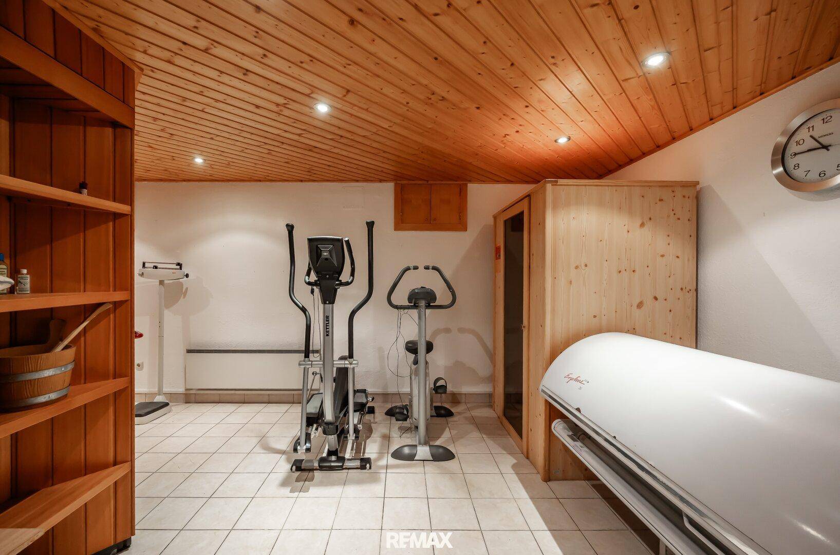 Fitnessraum mit Trainingsgeräten, Holzdecke und integrierter Infrarotkabine.