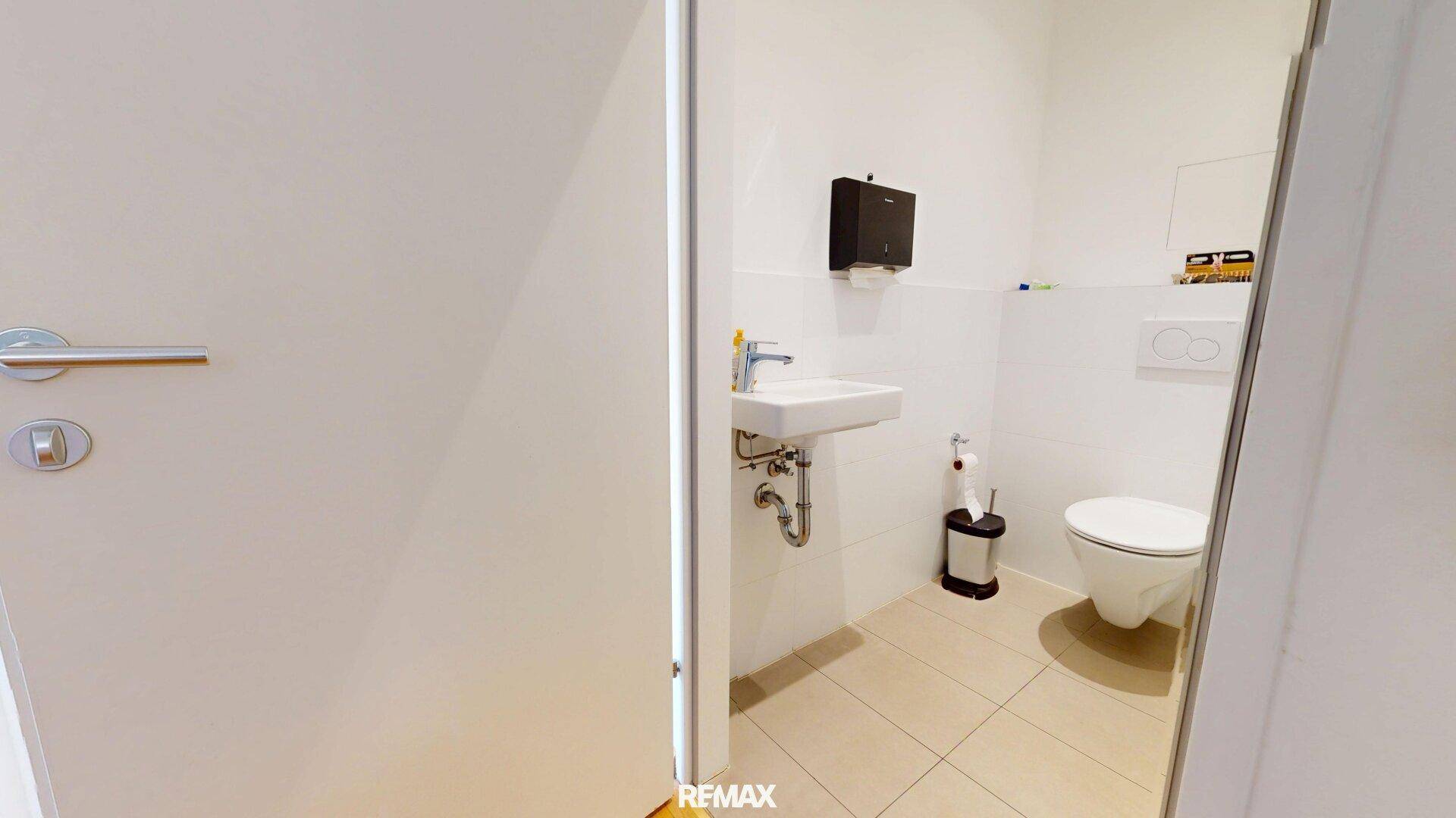 Kleines, modernes Badezimmer mit WC, Waschbecken und hellen Fliesen.