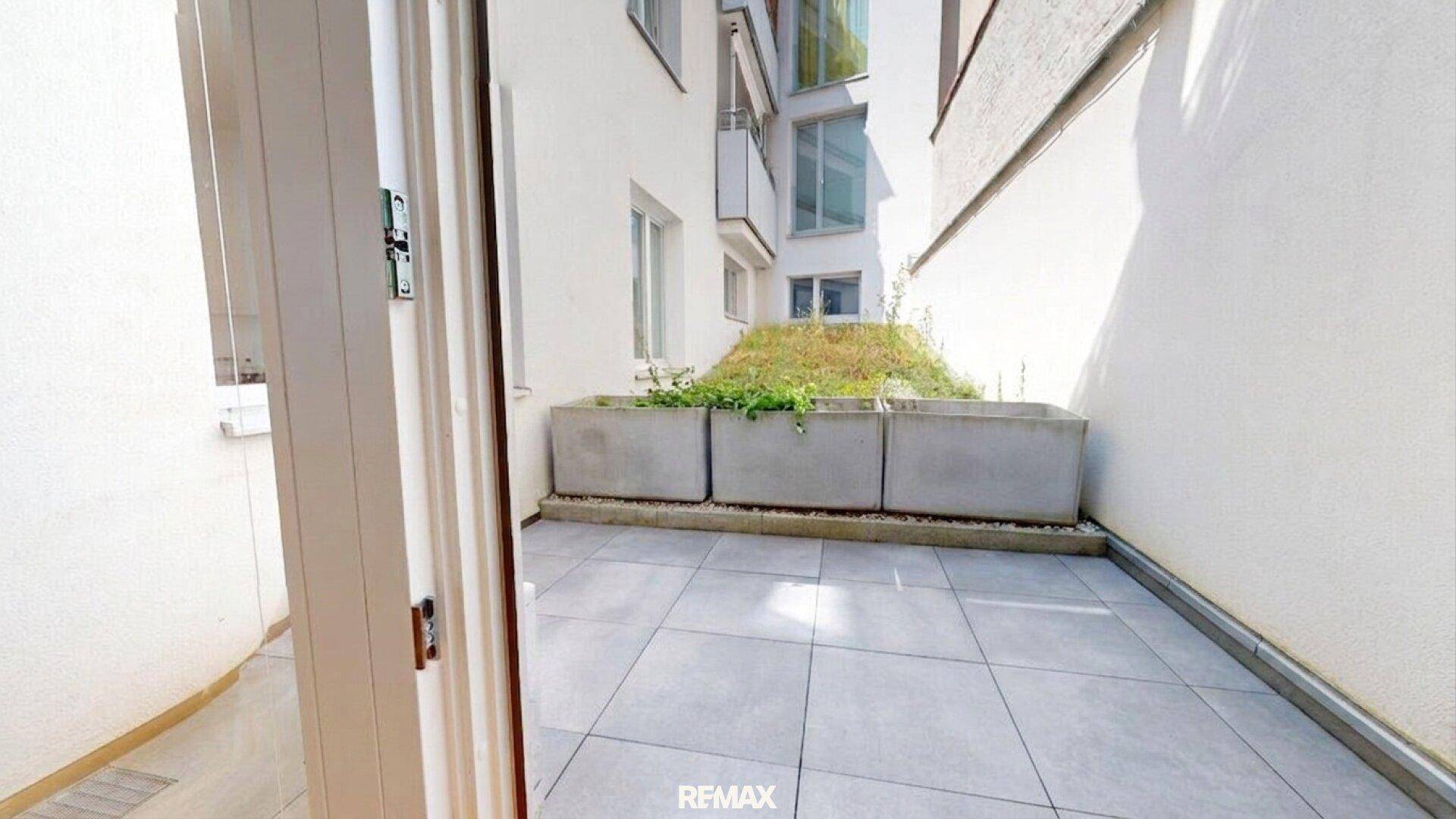 Kleine, geflieste Terrasse mit Pflanzenkübeln und Blick auf den Innenhof.