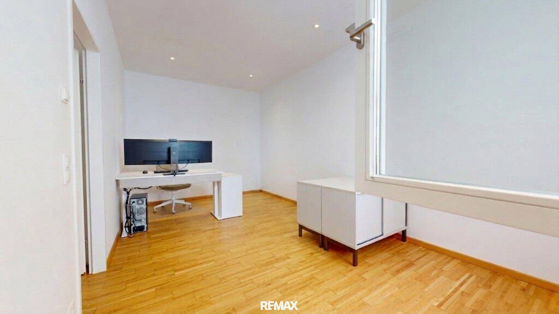 Funktional eingerichtetes Büro mit Schreibtisch, zwei Monitoren und Holzfußboden.