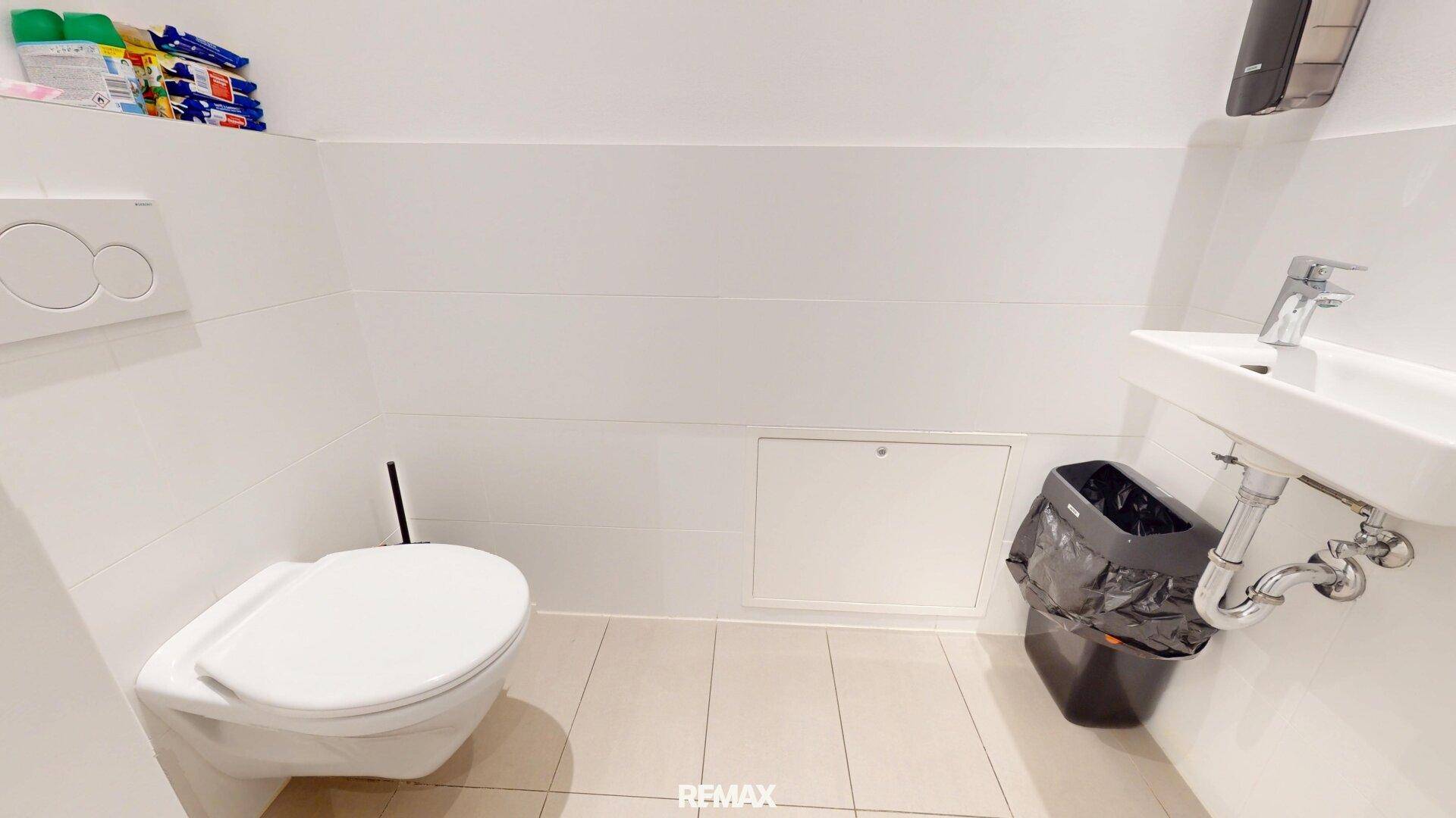 Separate Toilette mit Wand-WC, kleinem Waschbecken und Fliesenboden.