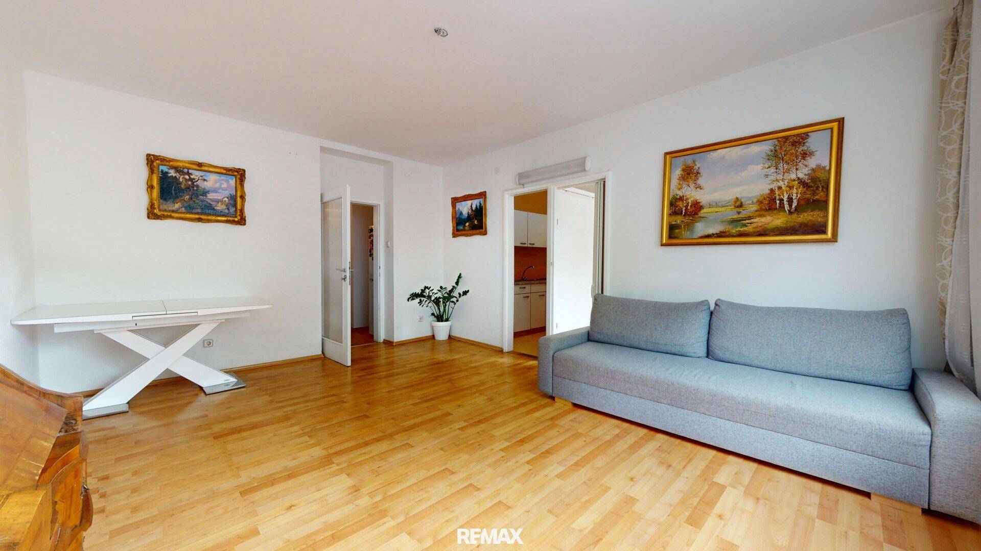 Geräumiges Wohnzimmer mit hellem Parkettboden, einem Sofa und klassischer Dekoration.