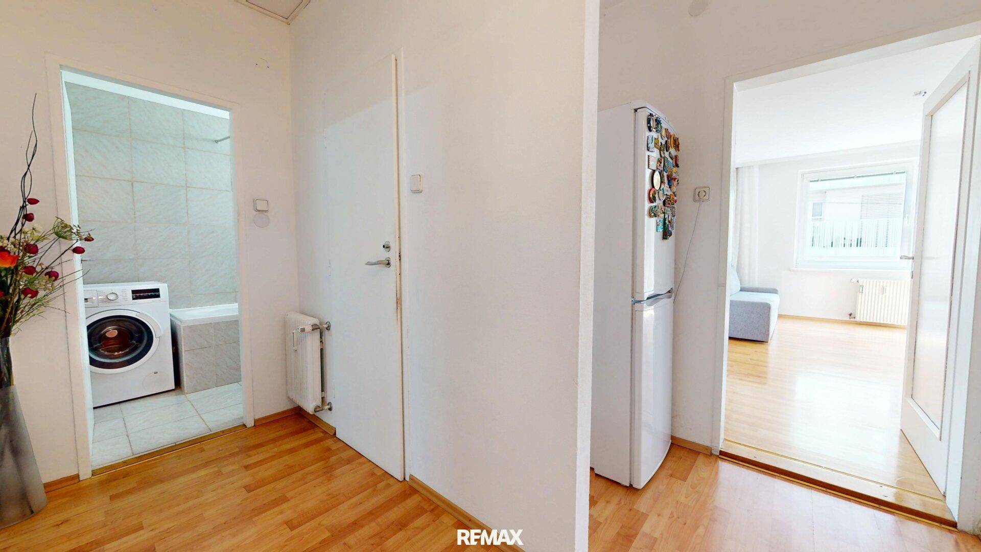 Flurbereich mit Parkettboden, einem Kühlschrank und Zugang zum Badezimmer mit Waschmaschine.