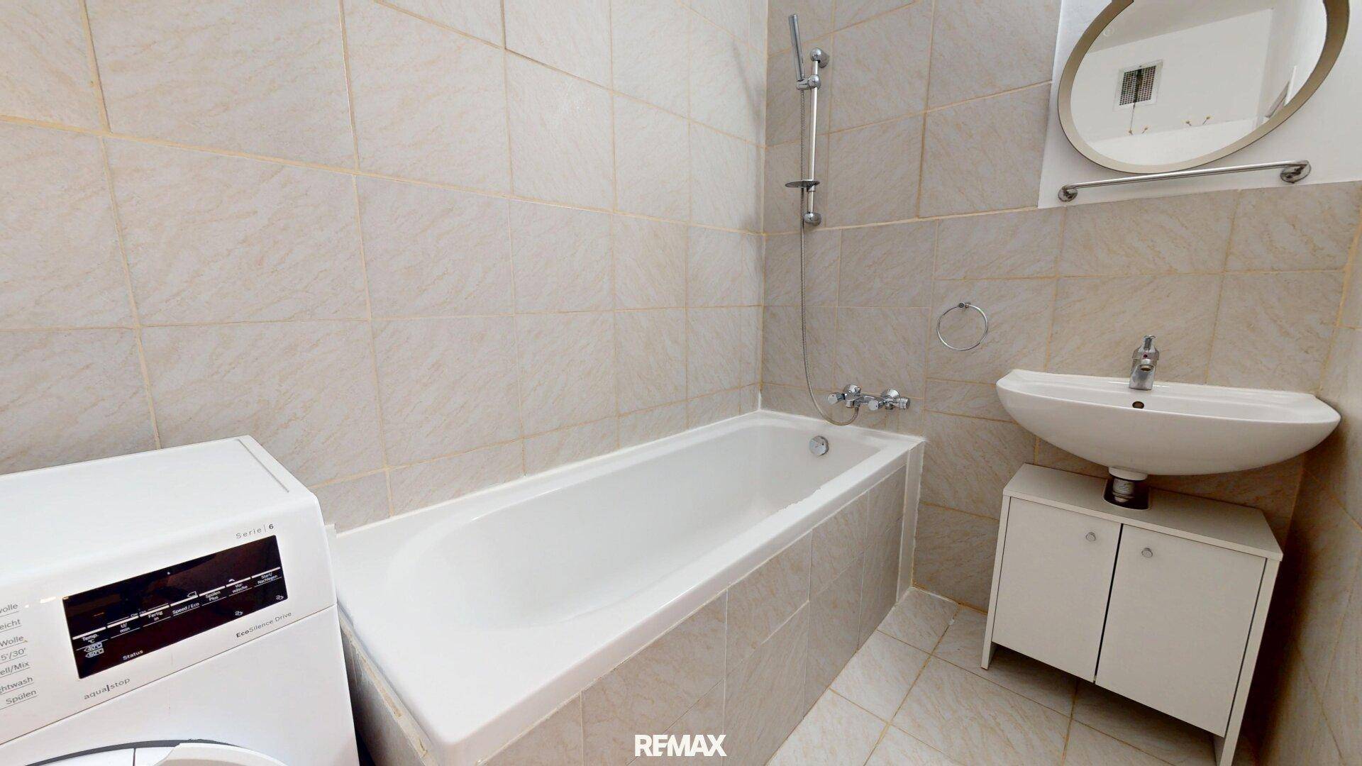 Badezimmer mit Badewanne, Waschbecken, Spiegel und einer Waschmaschine.